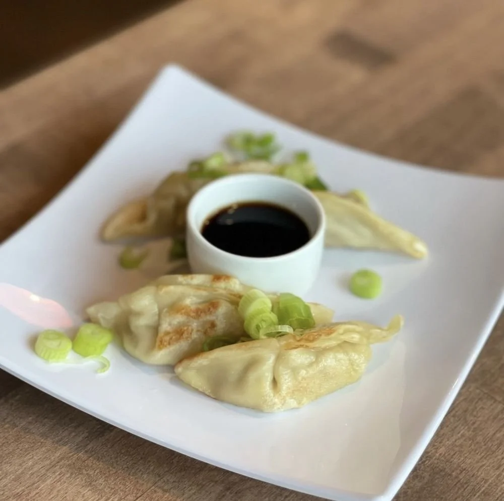 Dumplings with dipping sauce on a white plate, garnished with chopped green onions.