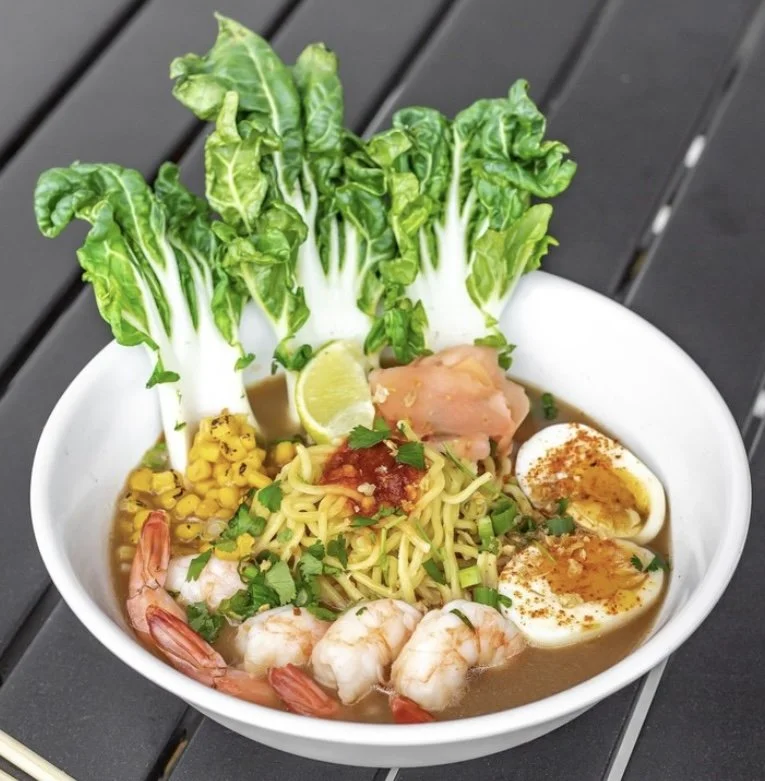 Bowl of seafood ramen with shrimp, boiled eggs, noodles, corn, lettuce, lime, and sliced chicken
