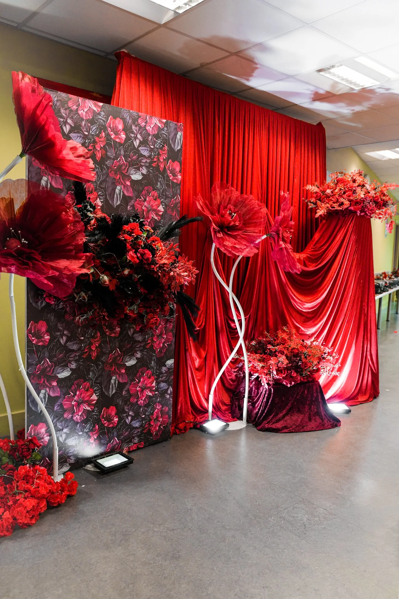 Red wedding or event backdrop with floral arrangements, draped red fabric, and decorative elements.