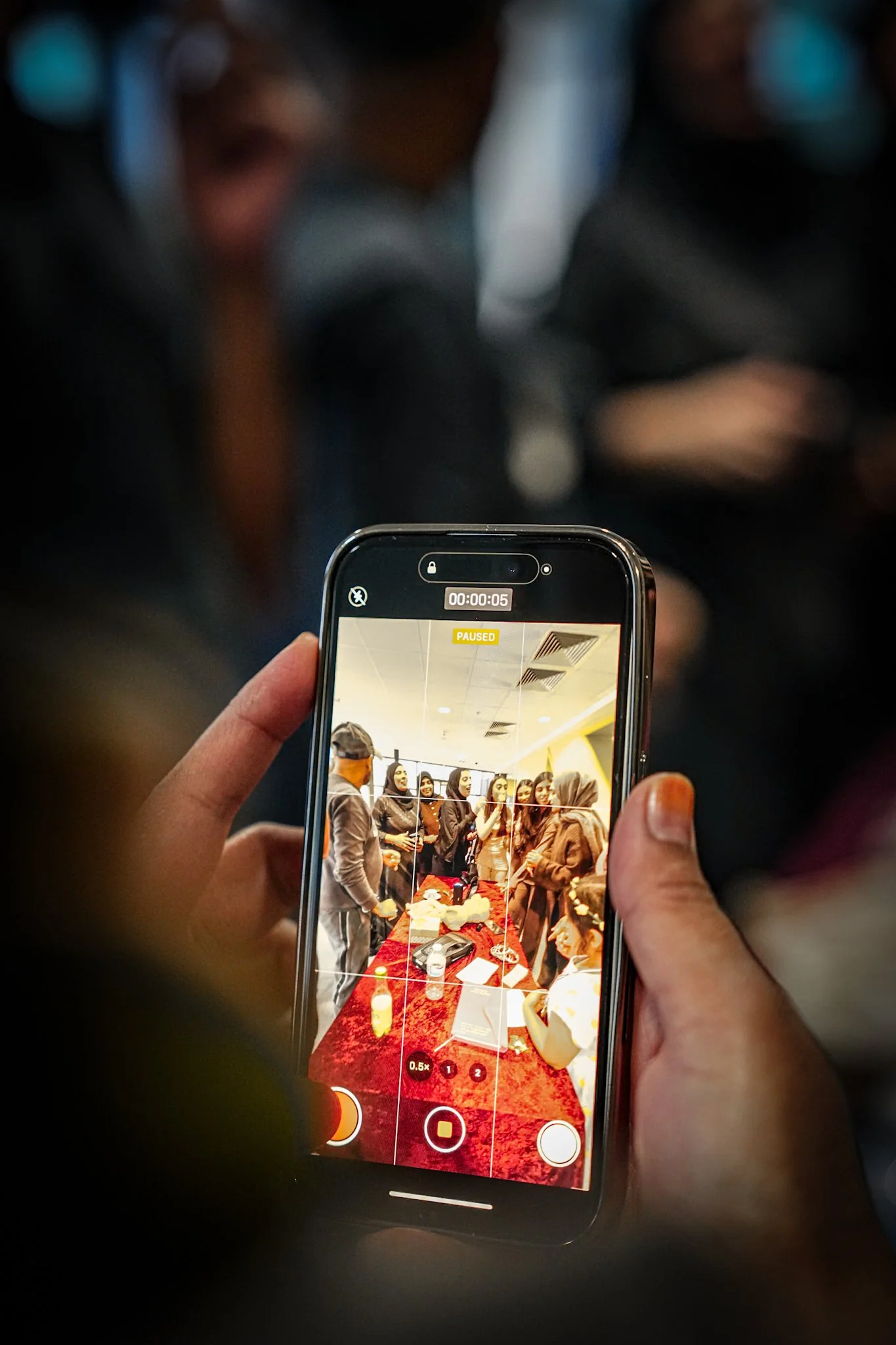 A person taking a photo of a group of people gathered around a table with a red tablecloth in an indoor setting.