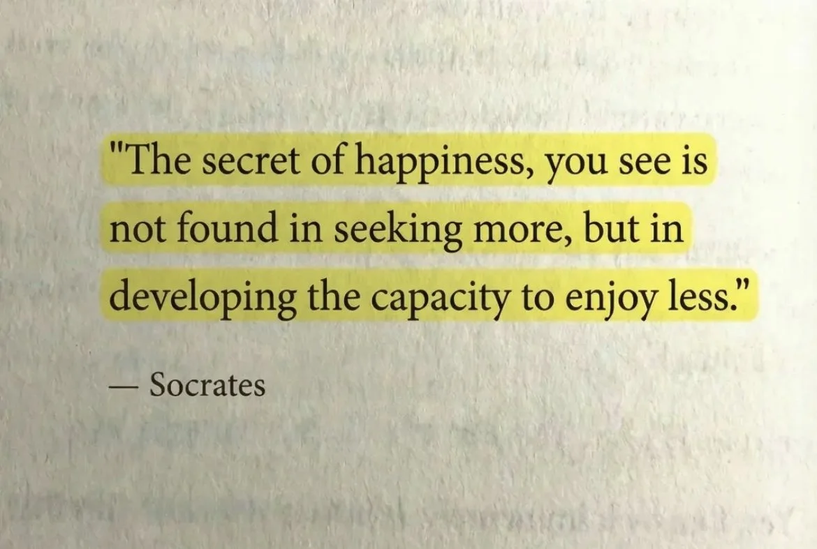Book page with a quote by Socrates highlighted in yellow: 'The secret of happiness, you see is not found in seeking more, but in developing the capacity to enjoy less.'