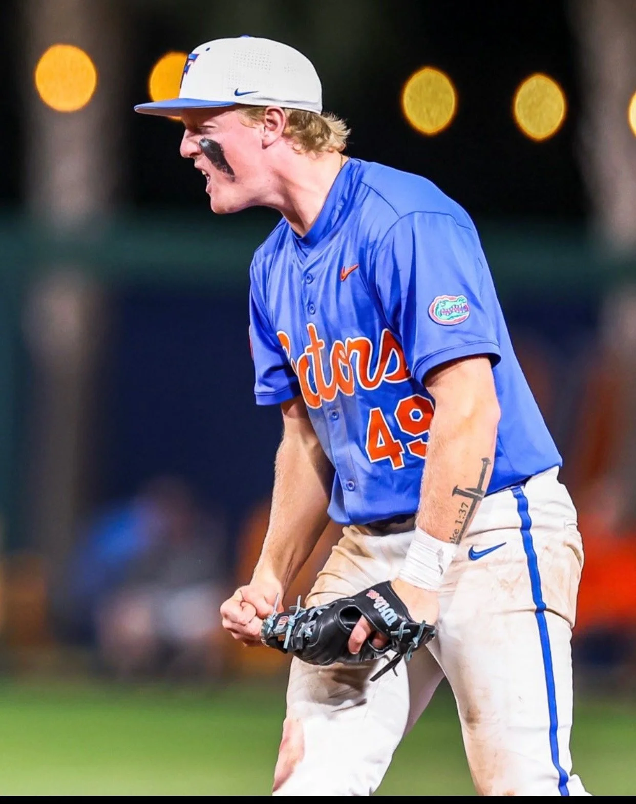 A baseball player wearing a blue University of Florida jersey with the number 49, white pants, and a grey cap is celebrating on the field during a game.