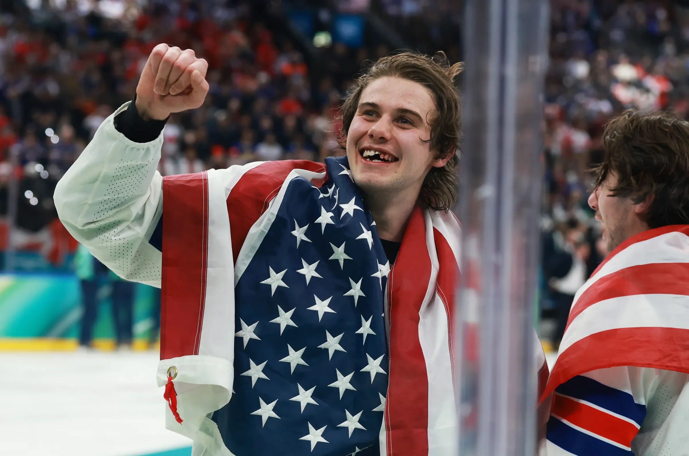 Ice hockey players celebrating, one wearing an American flag towel, on ice rink with crowd in background.