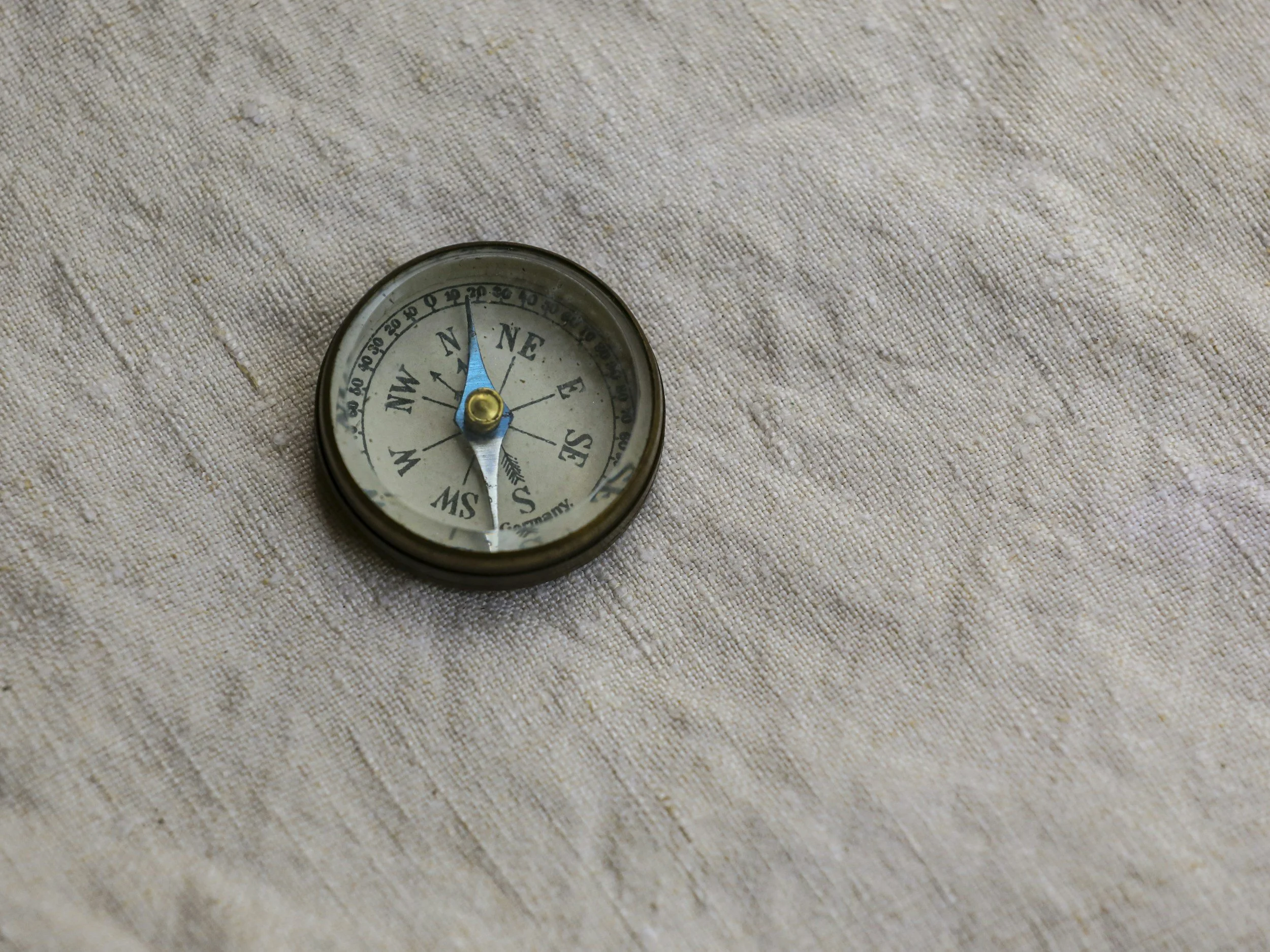 Small compass resting on beige textured fabric, representing direction and clarity