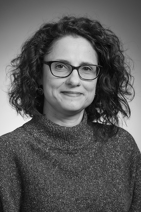 Black and white portrait of a woman with curly hair, wearing glasses and a textured turtleneck sweater, against a plain background.