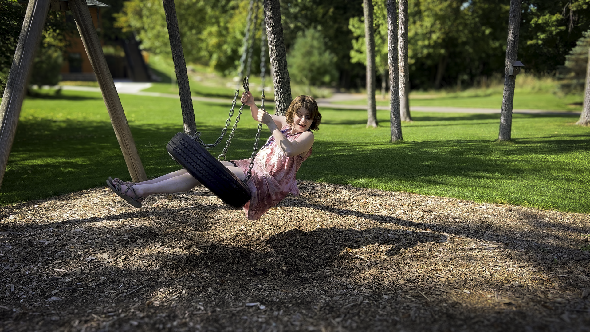 a woman with PWS smiling, wearing a dress, and swinging on a tire swing
