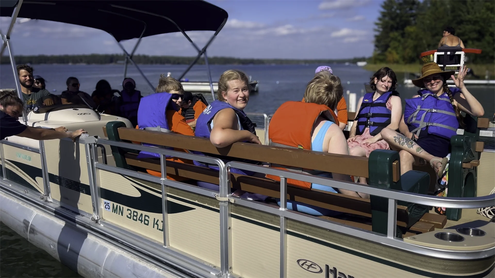 a group of people with pws on a pontoon ride, smiling, wearing life jackets
