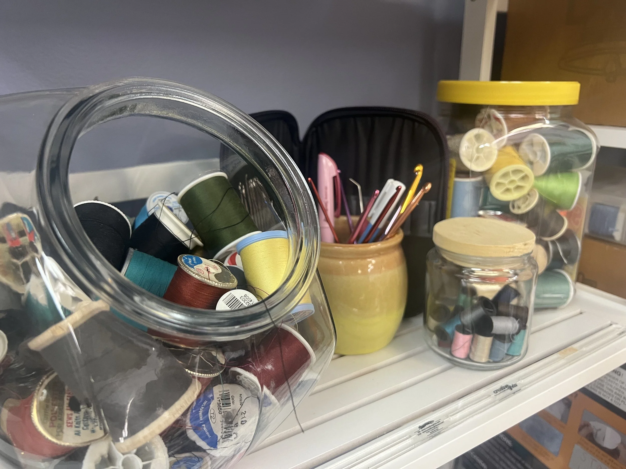 Closet shelf with jars containing various sewing supplies such as thread and other small sewing tools.