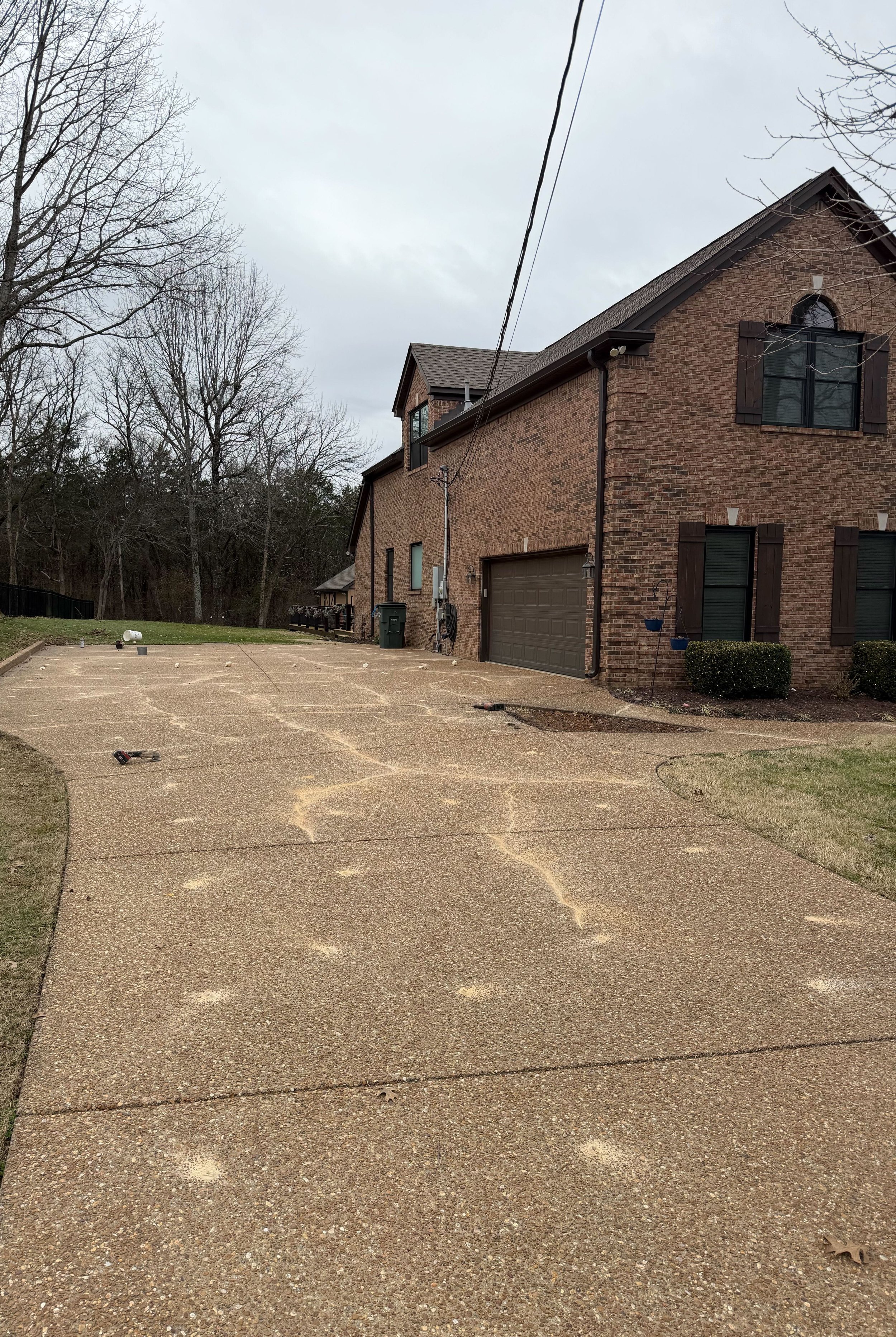 View of a house with a concrete driveway, visible footprints, and tools scattered on it, under an overcast sky.