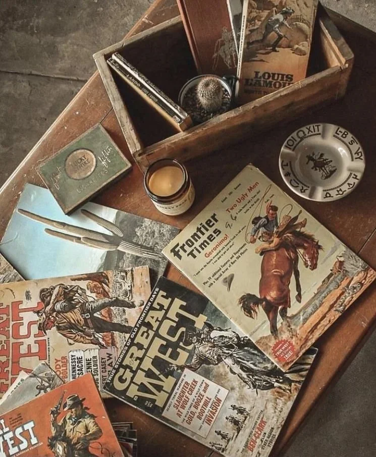 Vintage table with magazines, a candle, an ashtray, and a box containing books, a watch, and a photograph of a woman on horseback.