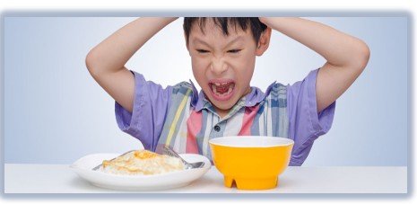 Frustrated boy grabbing his head and shouting at a table with a plate of eggs and a yellow bowl.