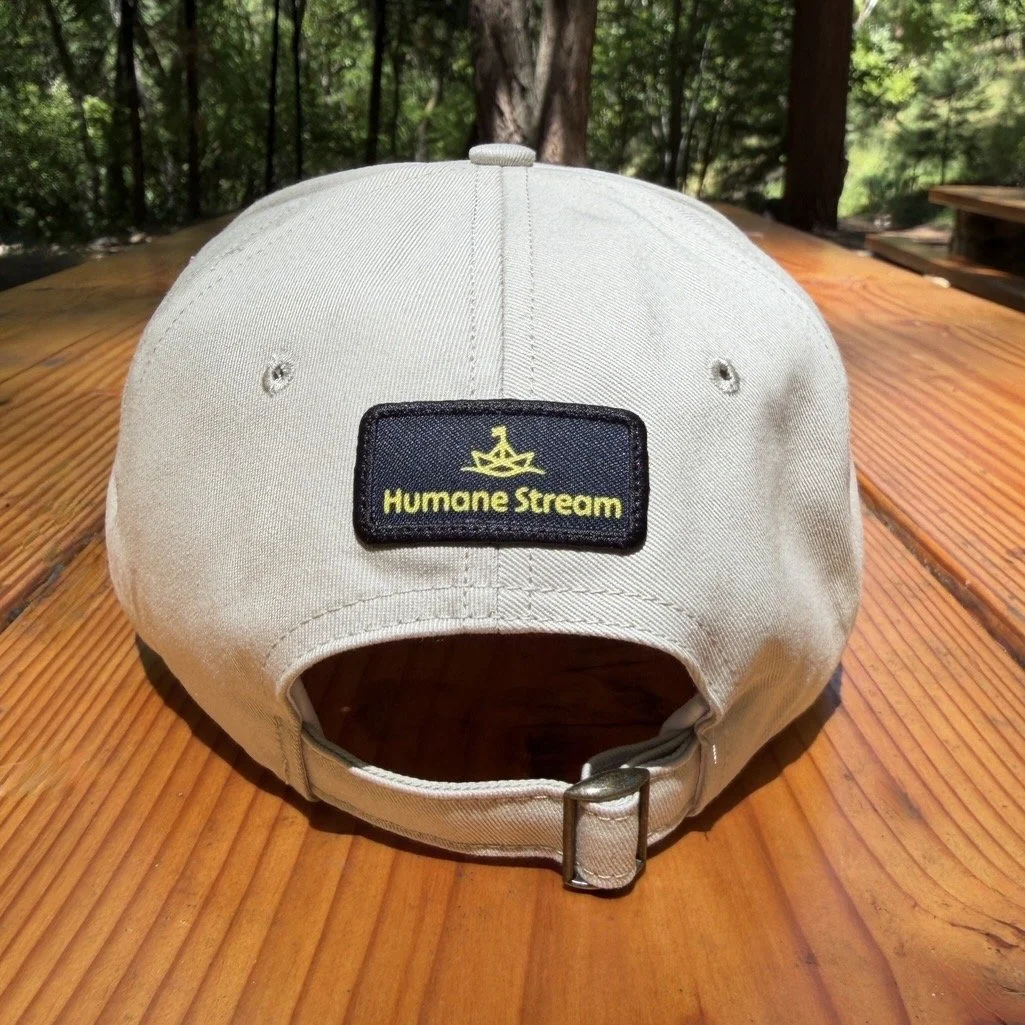 Image of the back of an off-white baseball cap with a Humane Stream logo