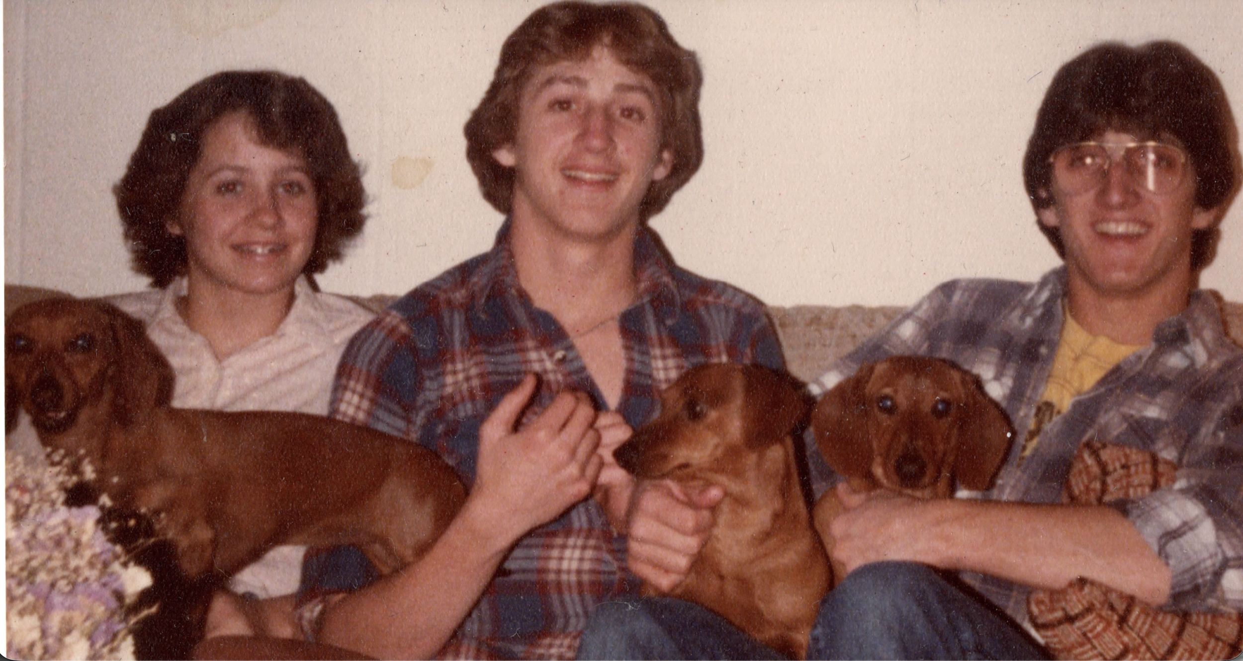 Three kids are sitting on a couch with their three dogs.
