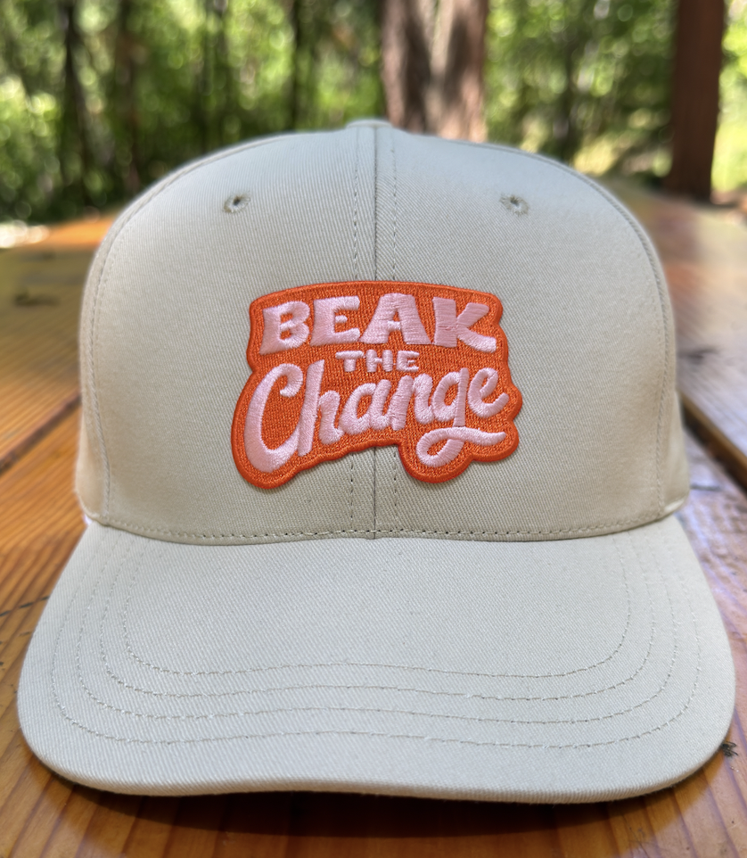 Image of an off-white baseball cap with a "Beak the change" message sitting atop a picnic table