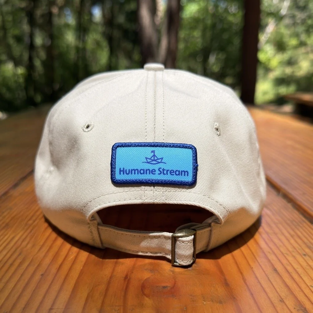 Image of the back of an off-white baseball cap with a Humane Stream logo