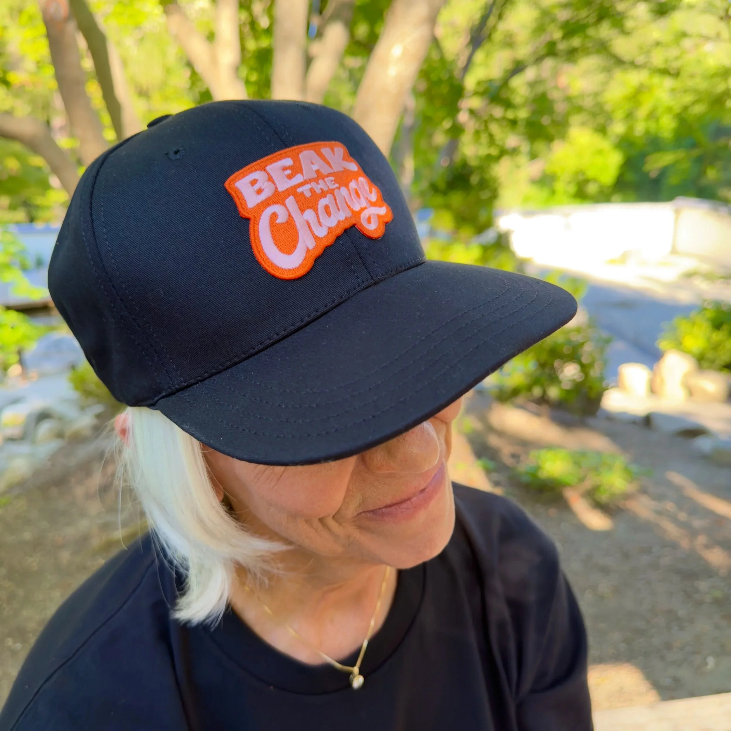 Image of woman wearing a black baseball cap that has the message: Beak the change