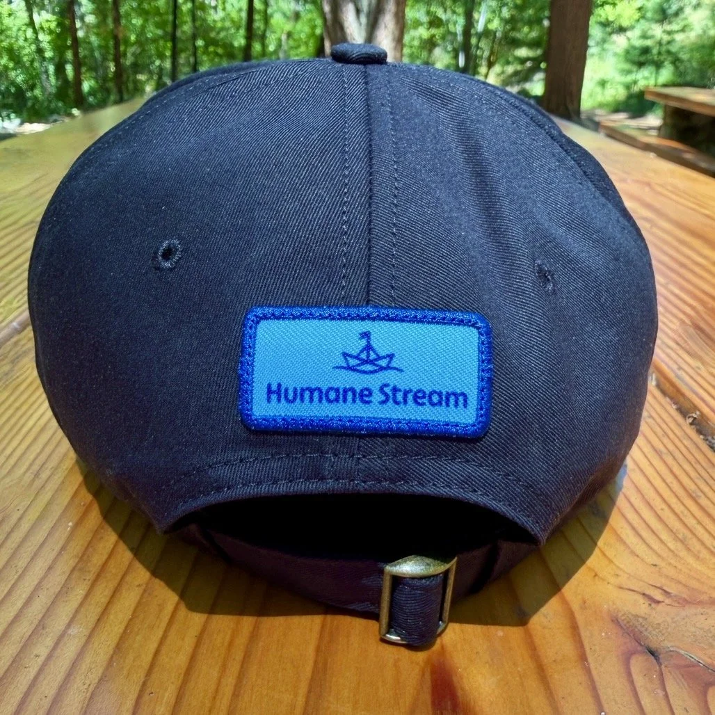 Image of the back of a black baseball cap with a Humane Stream logo