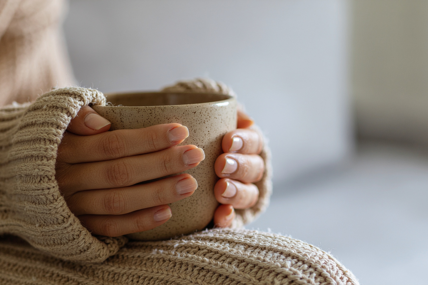 Close-up of hands in a cozy sweater holding a mug of tea or coffee.