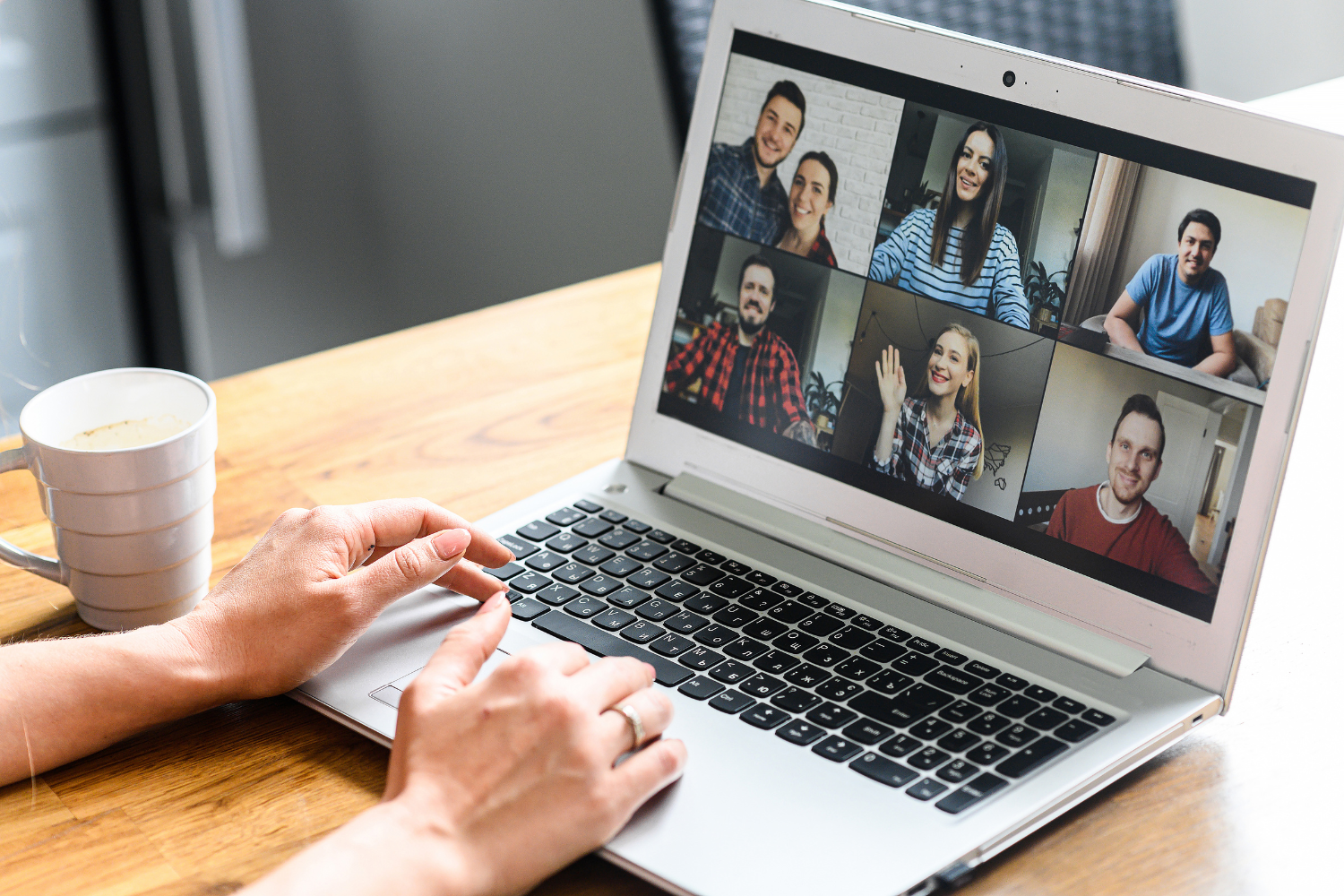 Hands on a laptop keyboard during a group video call with multiple participants