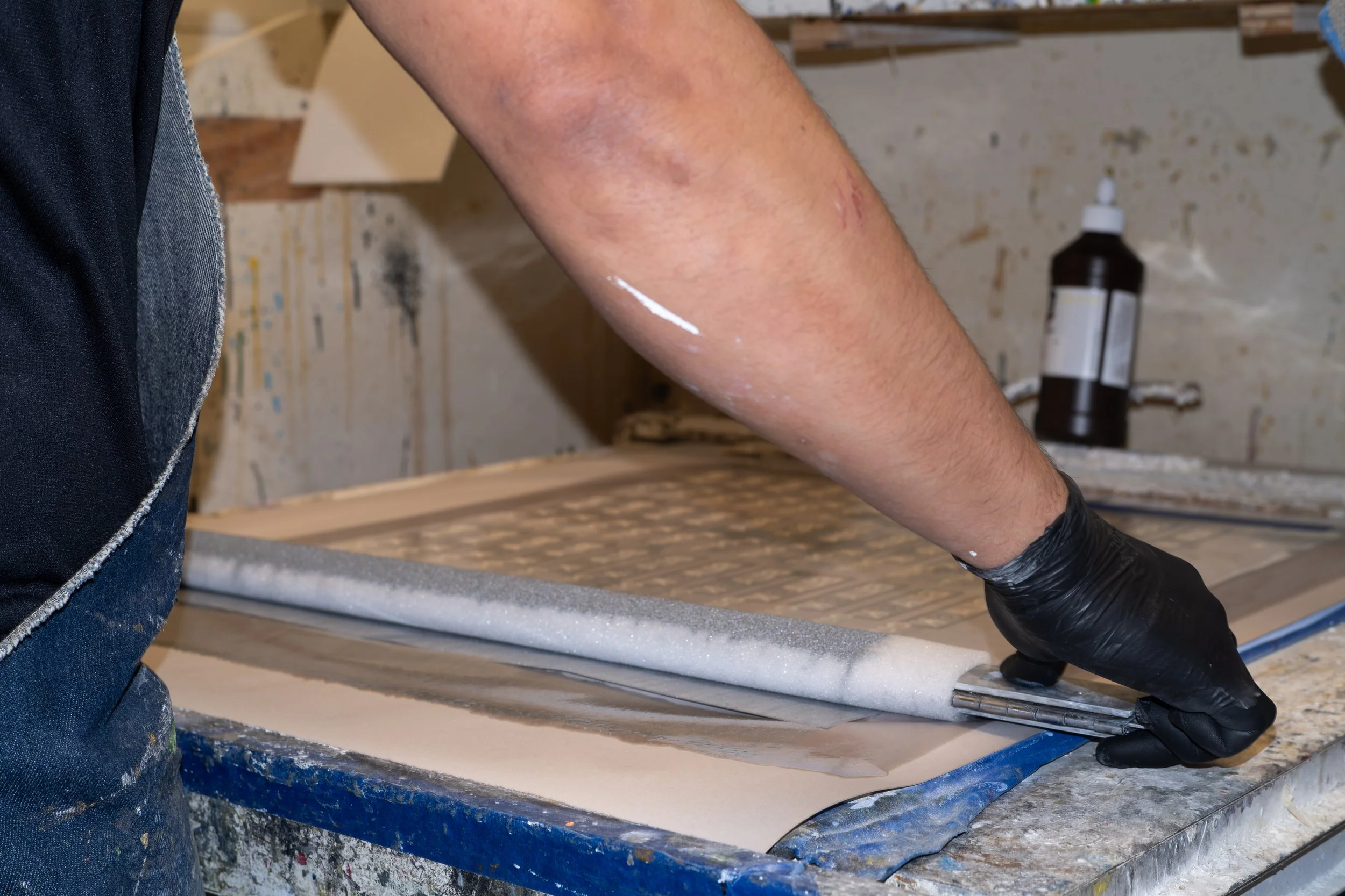 Person using a roller to apply adhesive to a foam sheet on a workbench in a workshop.