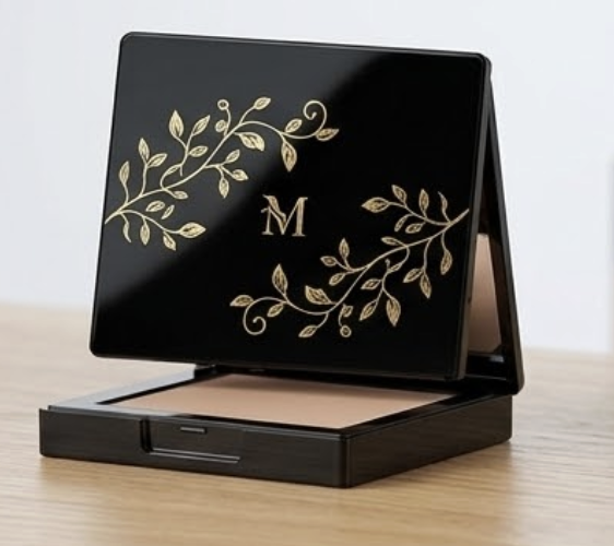 A black makeup compact with gold floral designs, a letter M, and an interior powder or blush.