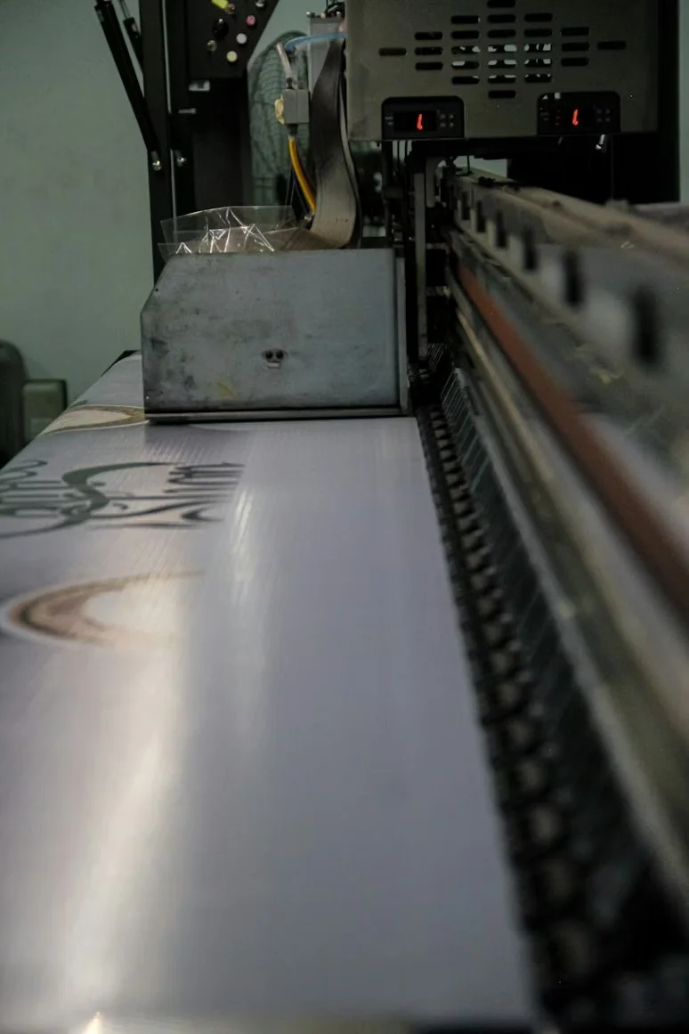 Close-up of a printing machine printing on a sheet of paper with a printed design, showing the printing mechanism and paper feeding process.