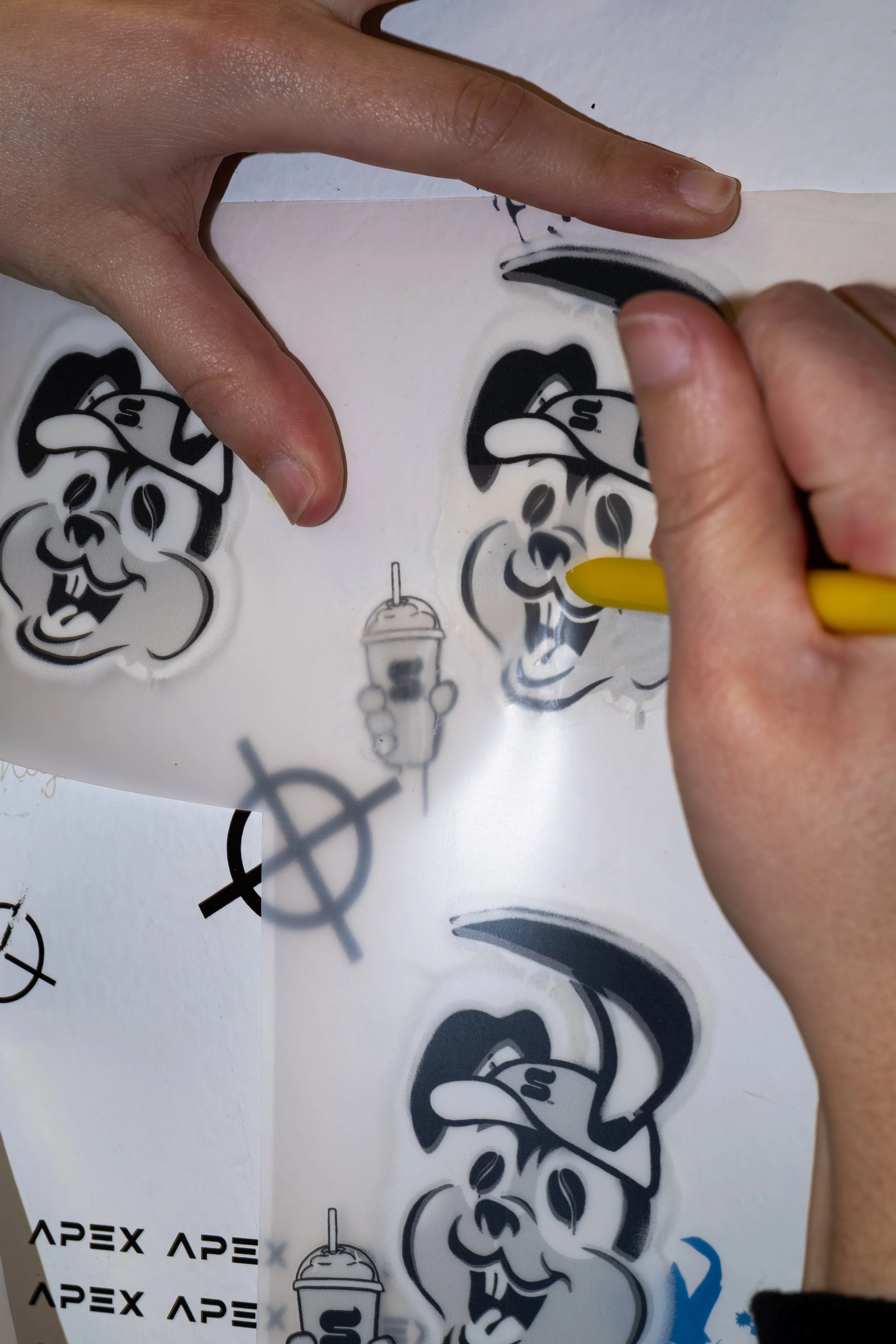 A person peeling Halloween pumpkin stickers with a ghost wearing a hat and a drink with a straw on a white surface.