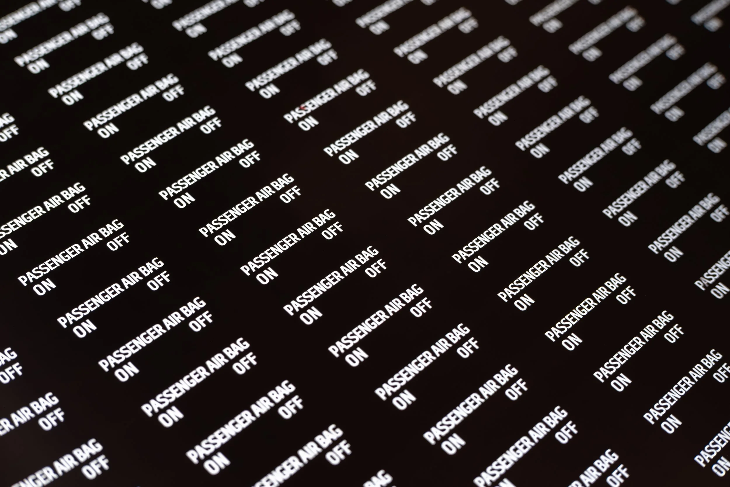 Black fabric with repeating white text pattern reading "PASSENGER AIR BAG ON" and "OFF".