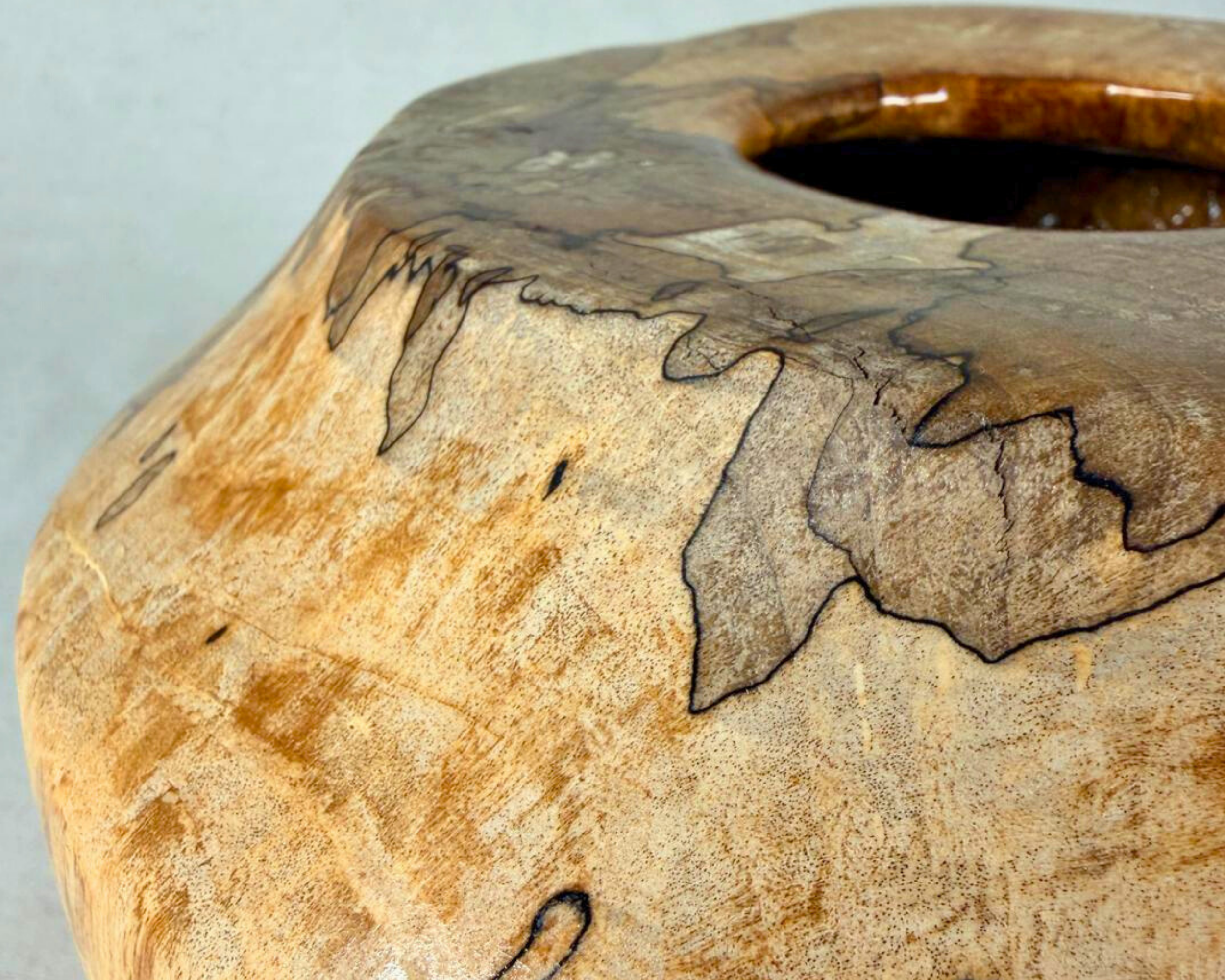 Close-up of the rim and upper shoulder of a spalted maple vessel, showing fine grain variation, pale maple tones, and dark spalting lines along the edge of the opening.