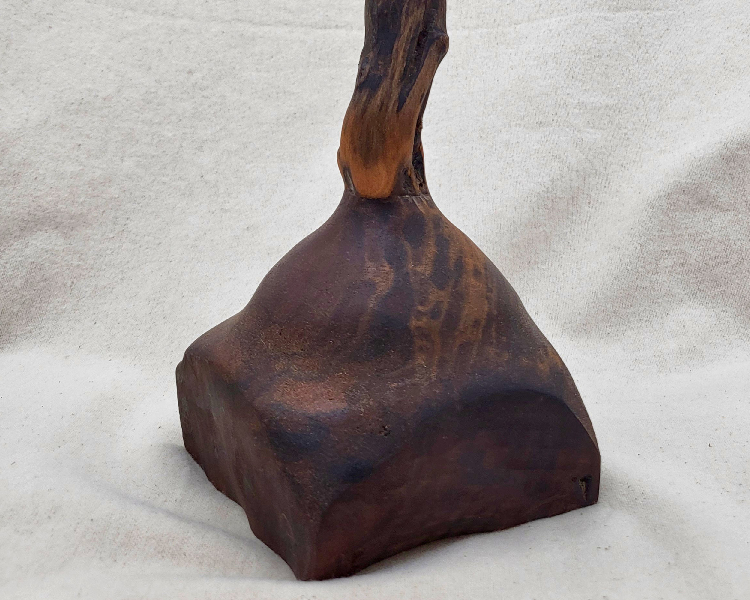 Detail of the claro walnut base on a sculptural wood piece by Treverk Woodturning, showing the deep chocolate-brown grain with darker streaks and warm amber undertones across the matte stone-like surface. Hand-turned organic wood art.