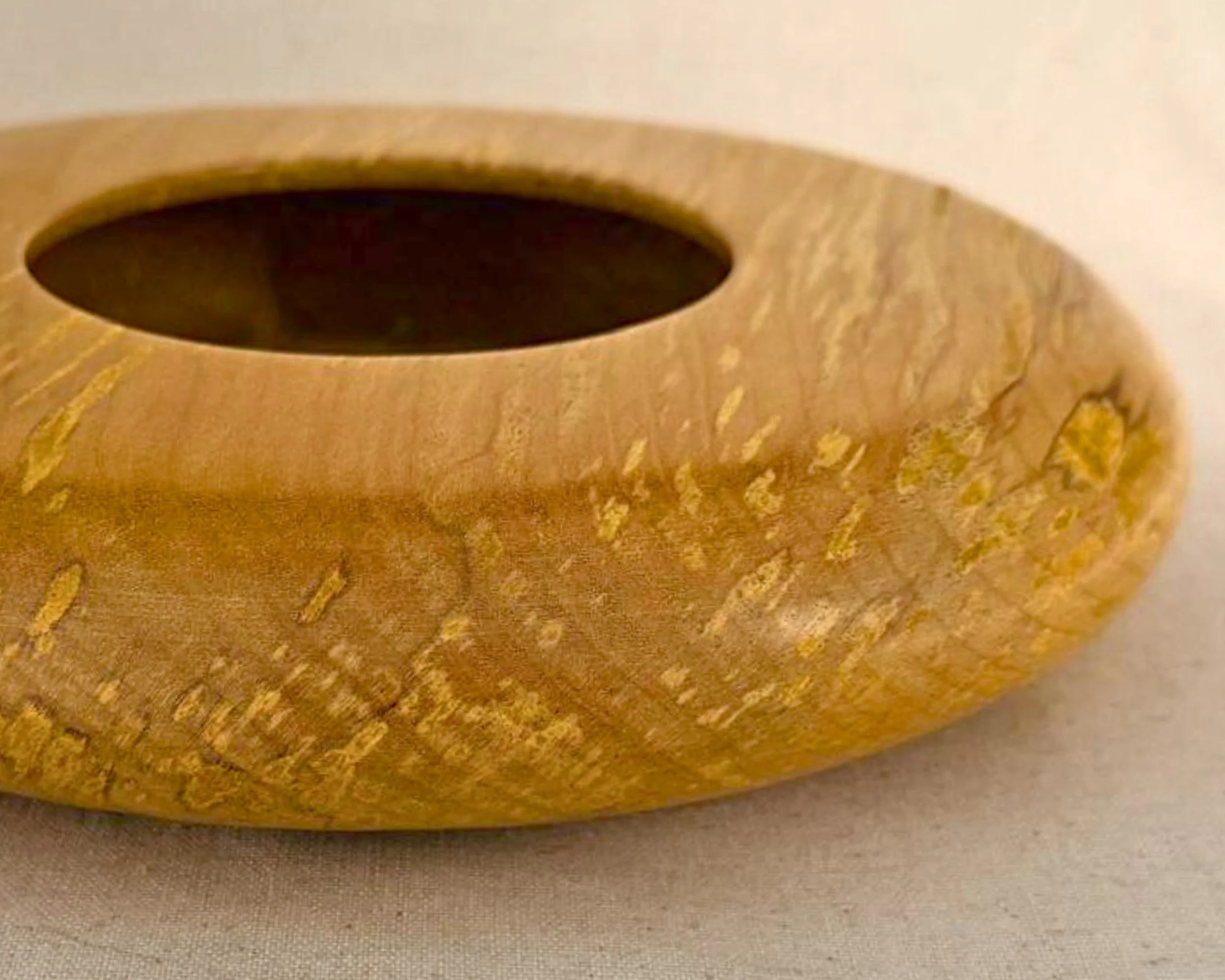 Detail view of figured maple surface on the closed form vessel showing character markings and flowing grain.