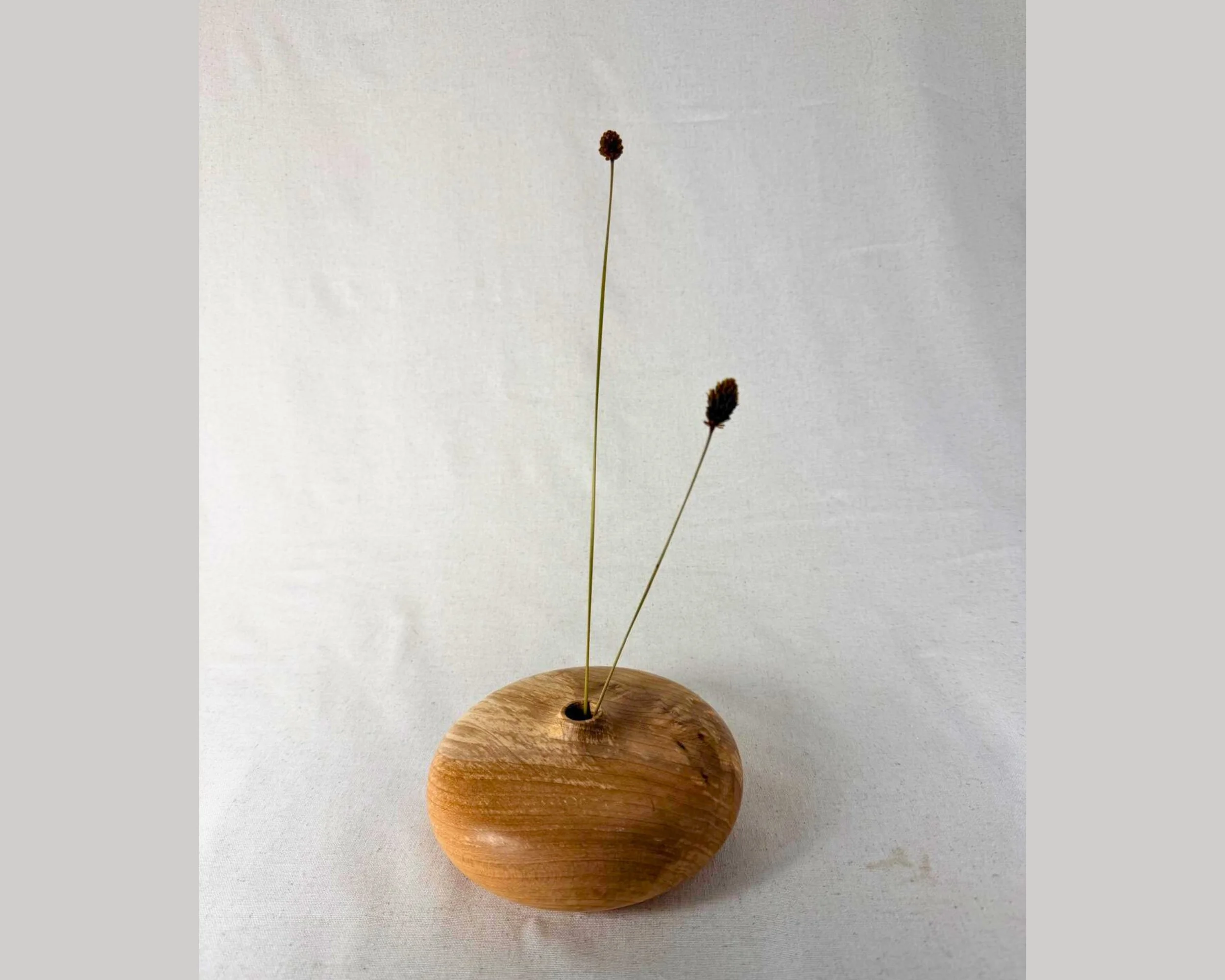 Figured maple closed form vessel styled with two dried stems placed in the small opening.