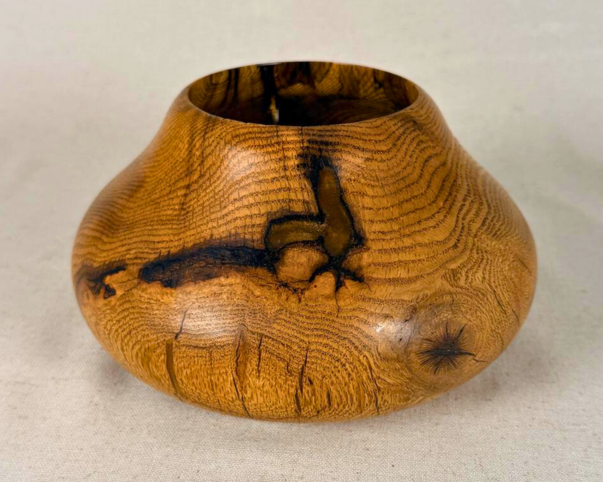 Hand-turned oak vessel, front view showing compact low form, natural checks and amber resin fills prominent across the front face, ray fleck grain throughout. One of a kind.