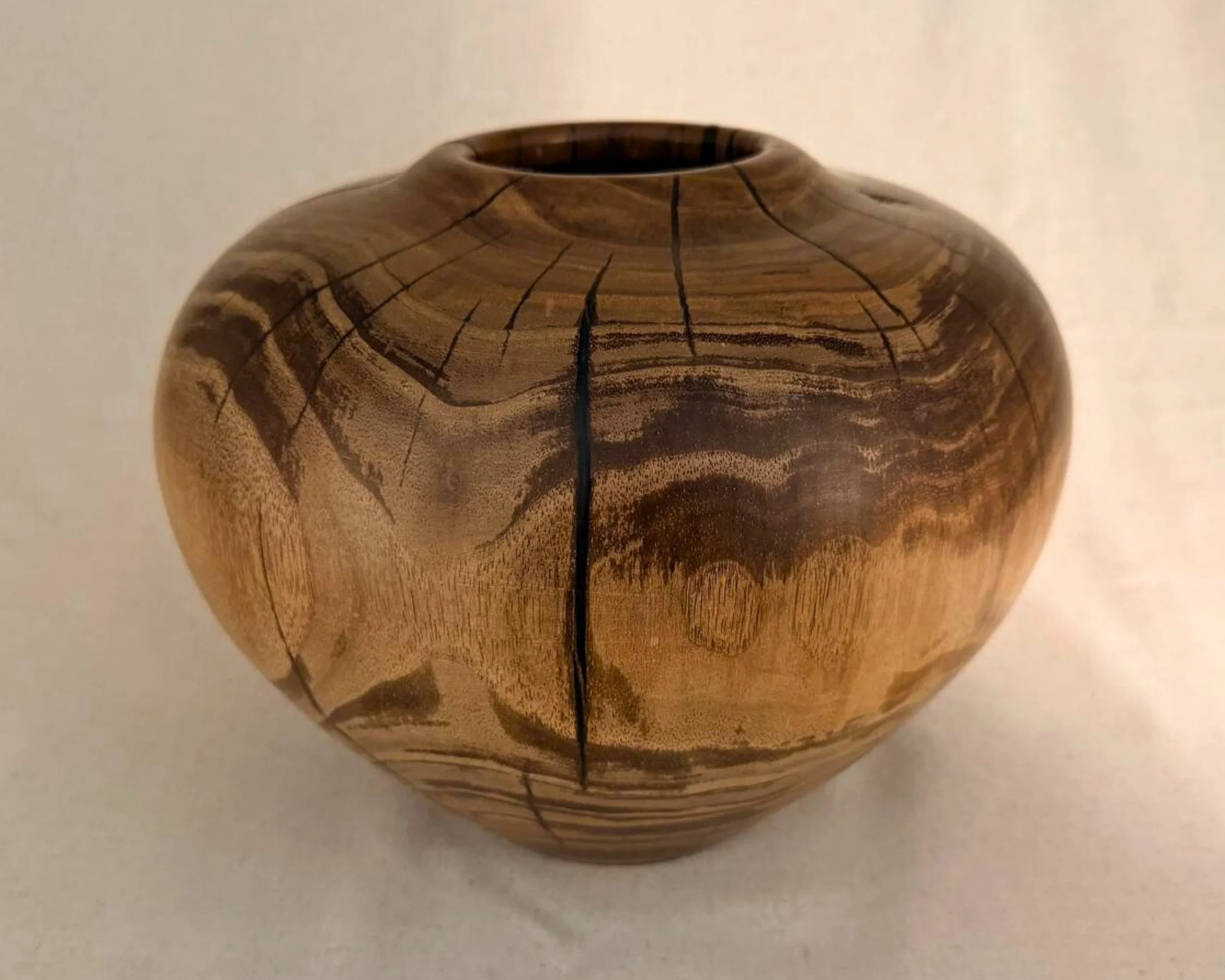 Hand-turned walnut vessel showing dramatic tree-grain bands and fine checking lines, front view on light background.