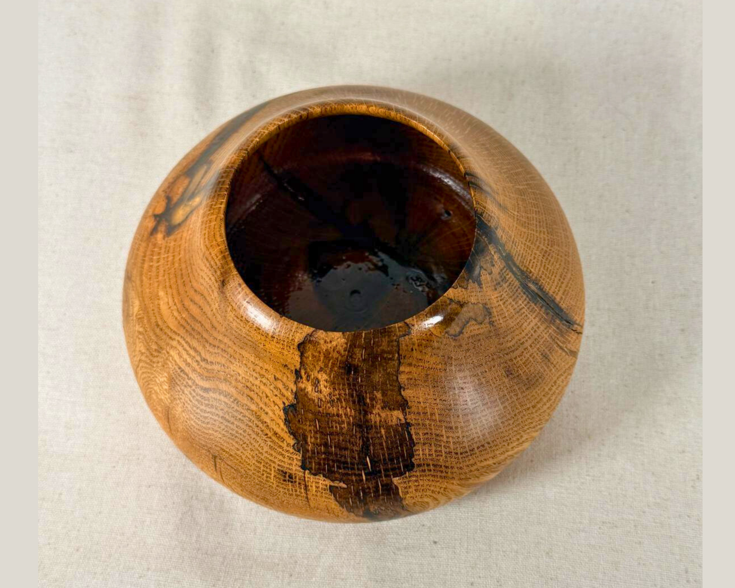 Angled overhead view of a hand-turned oak vessel, 3-inch opening visible, ray fleck grain and natural void edges radiating from center. Amber resin fills the checks. One of a kind.
