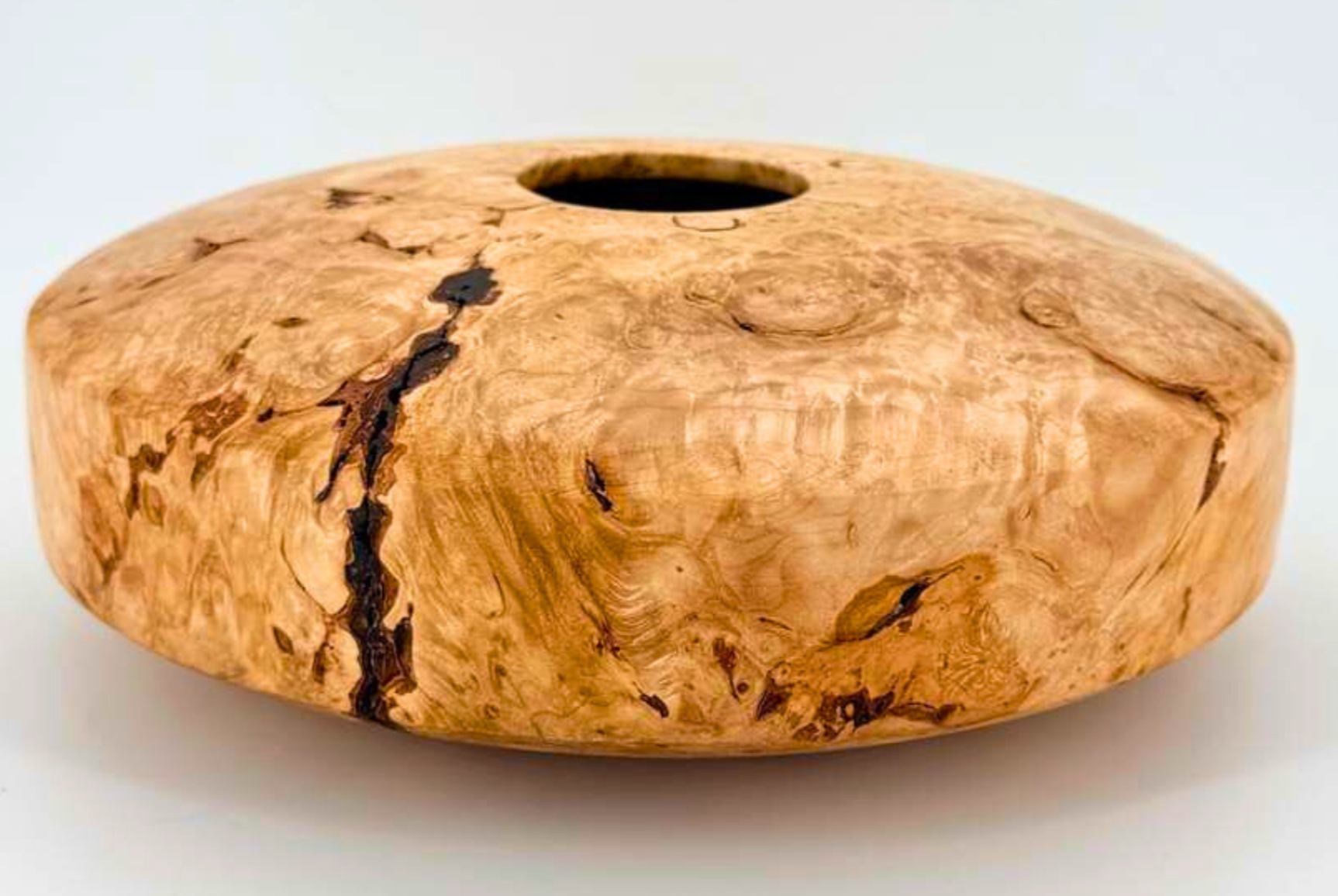 A round wooden tissue box holder with a hole in the center, made from burl wood with natural grain and dark streaks.