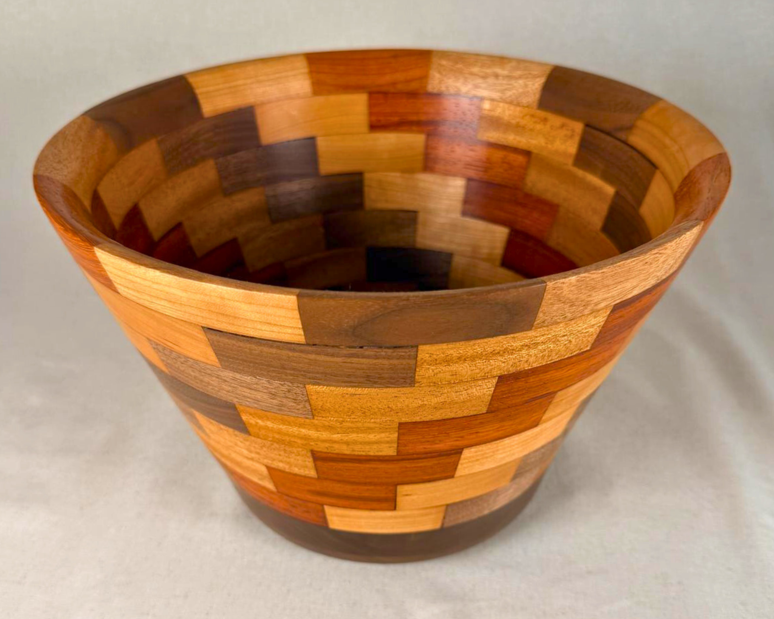 Angled top view of the segmented wood vessel showing the flared profile, patterned interior, and rich mix of warm-toned hardwoods.