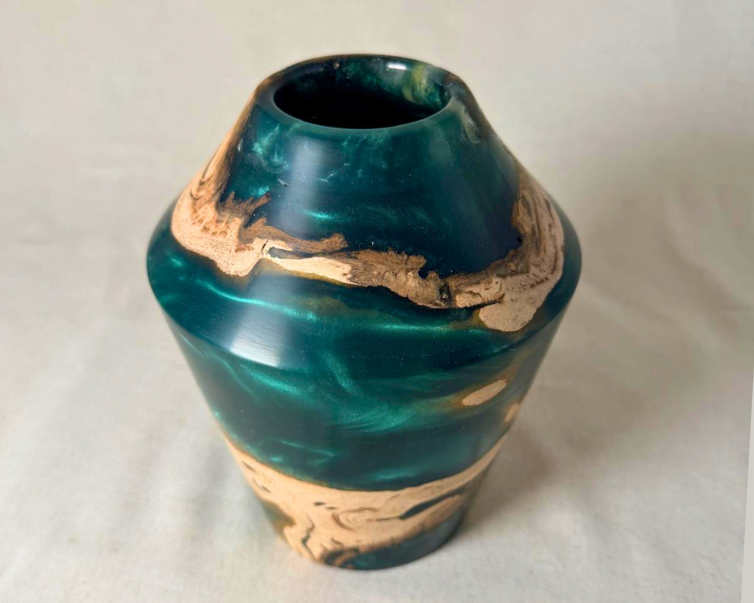 Hand-turned driftwood and green epoxy vessel in angled view with a narrow opening, faceted shoulder, and swirling natural wood patterns against translucent green resin.