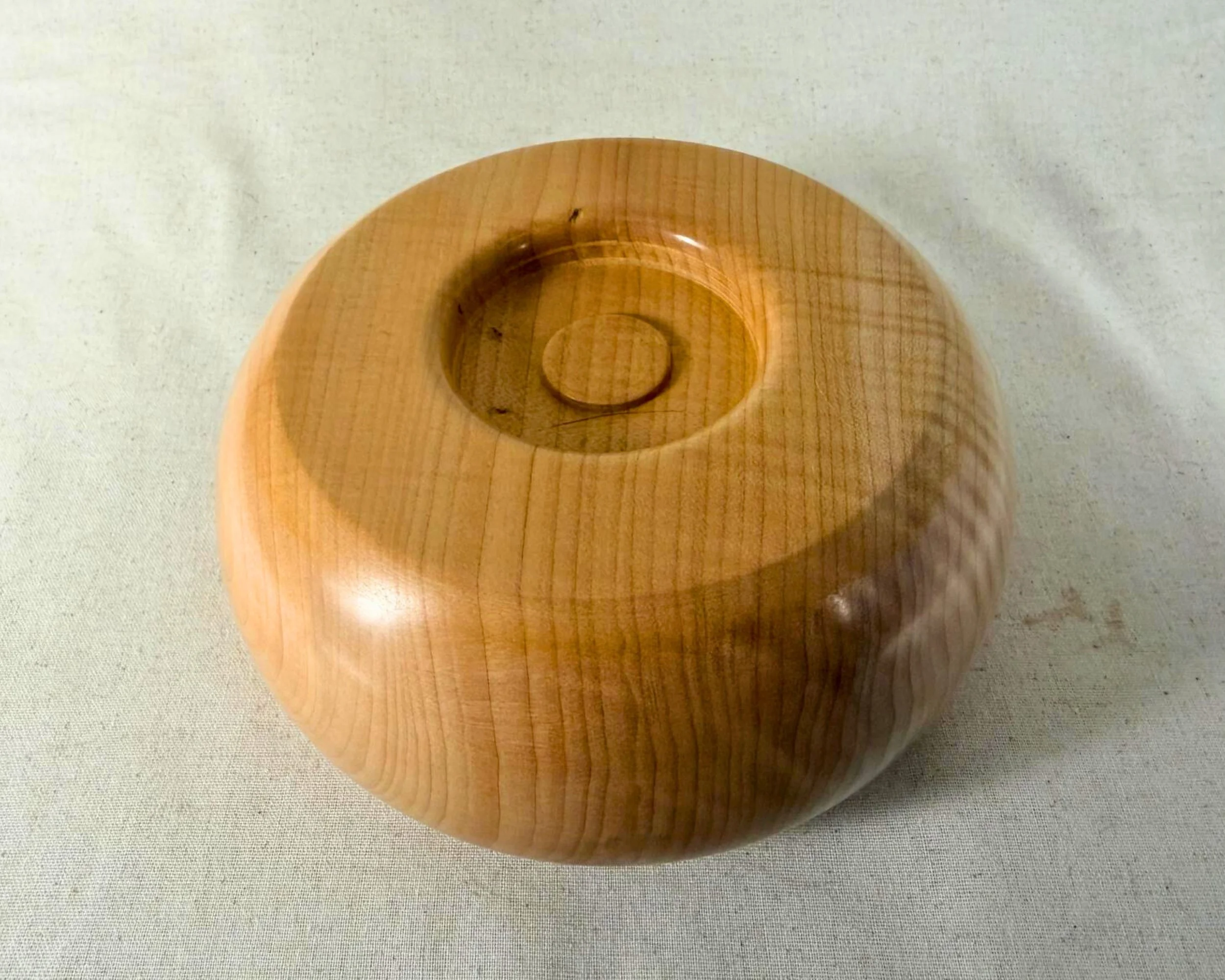 Underside of a hand-turned maple closed form vessel showing a recessed foot and smooth honey-toned finish.