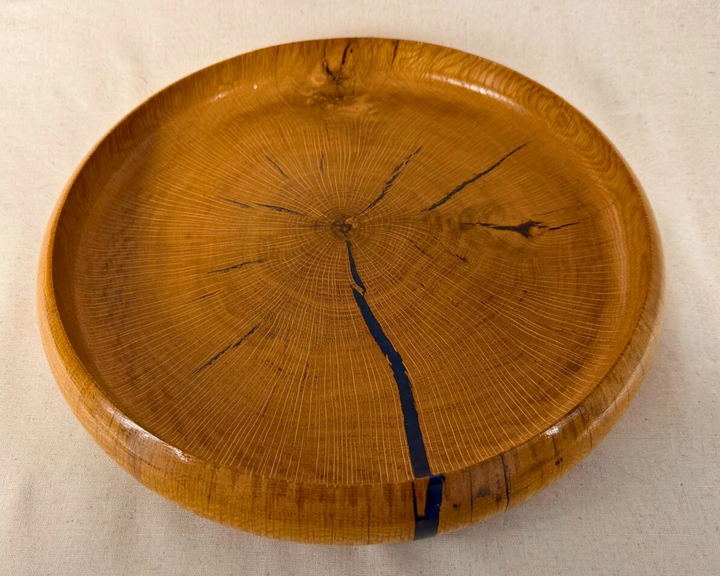 Top-down view of a reclaimed oak platter with dark blue epoxy lines running through natural checking, glossy finish.