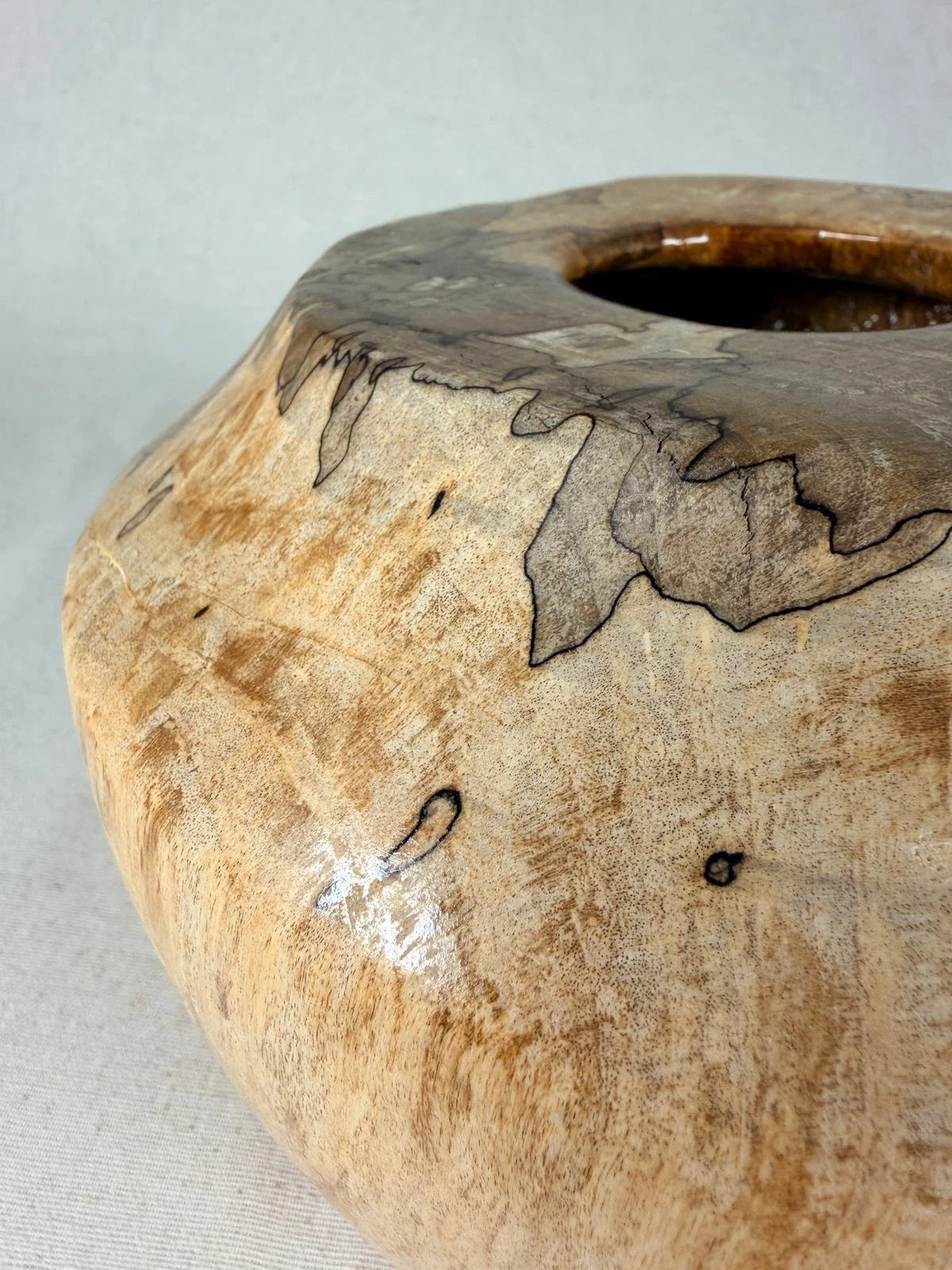 Spalted maple vessel shown at an angle, highlighting the broad rounded form, small centered opening, and dramatic dark spalting that travels across the rim and shoulder.