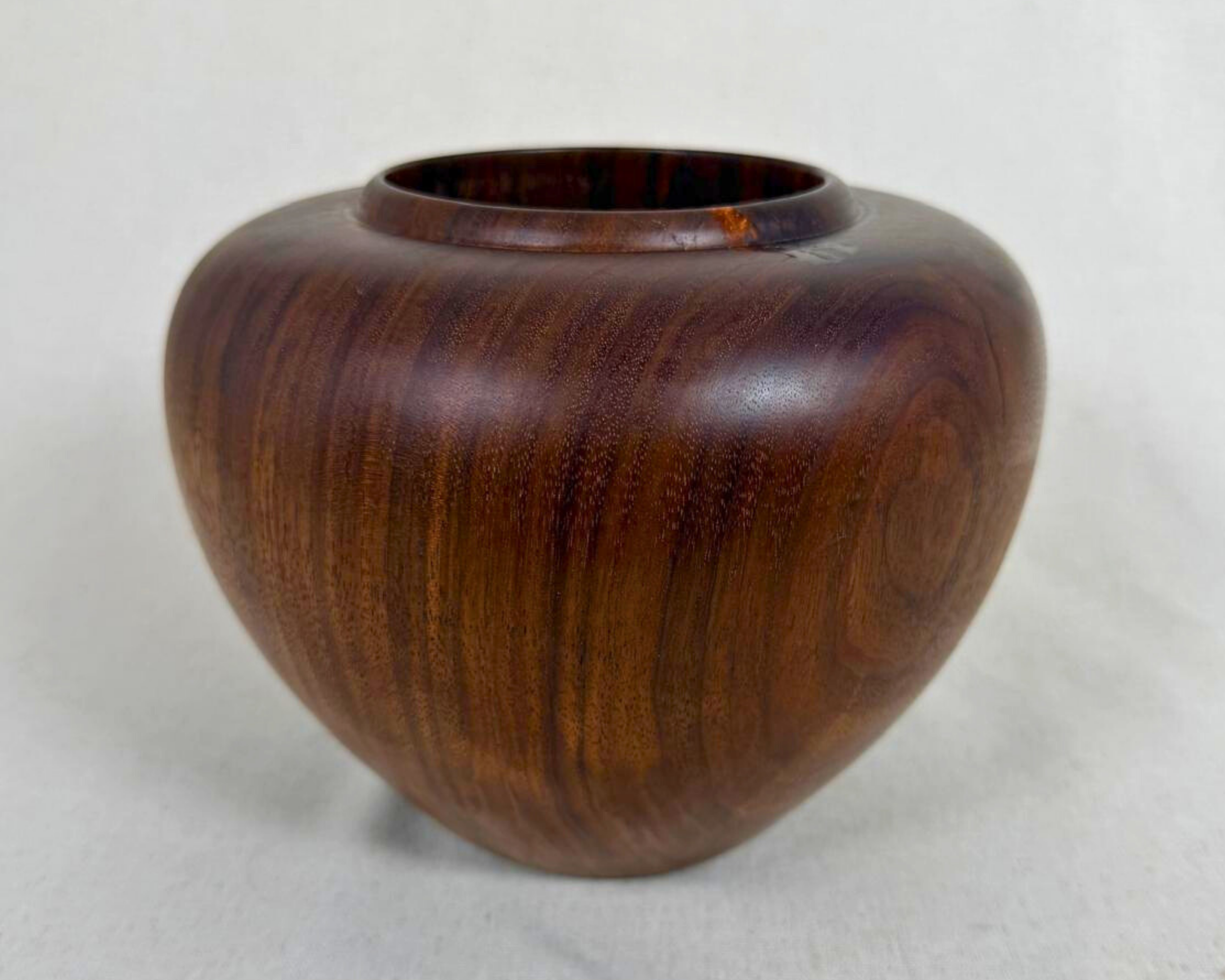 Front view of a hand-turned dark wood vessel with warm brown figuring, rounded body, and a small amber-toned natural inclusion near the rim.