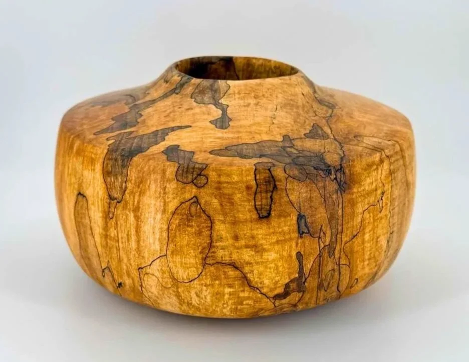 Wooden vase with a round shape and black grain pattern on a white background.