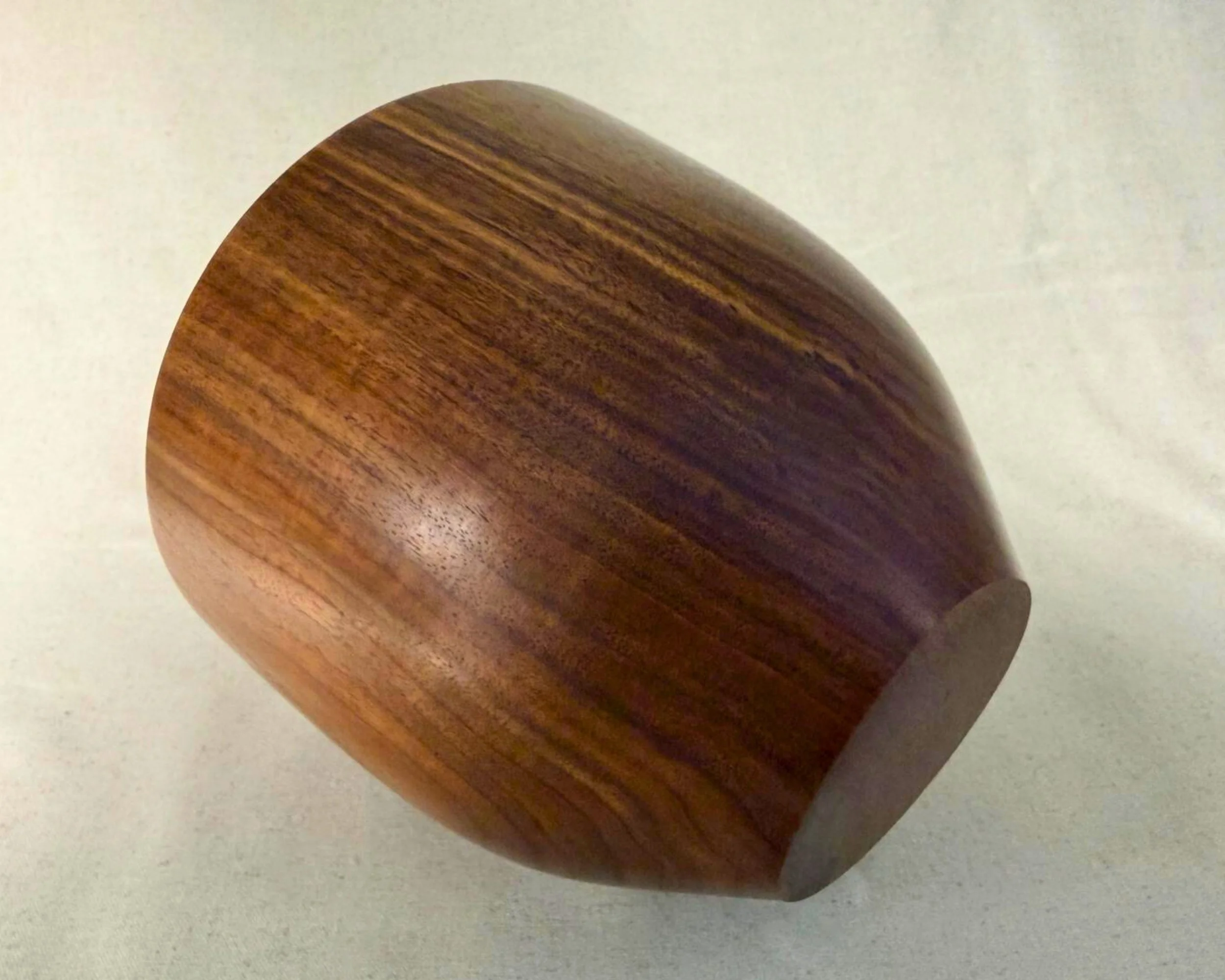 Tilted view of walnut vessel showing curved base, continuous turning lines, and strong grain movement along the body.