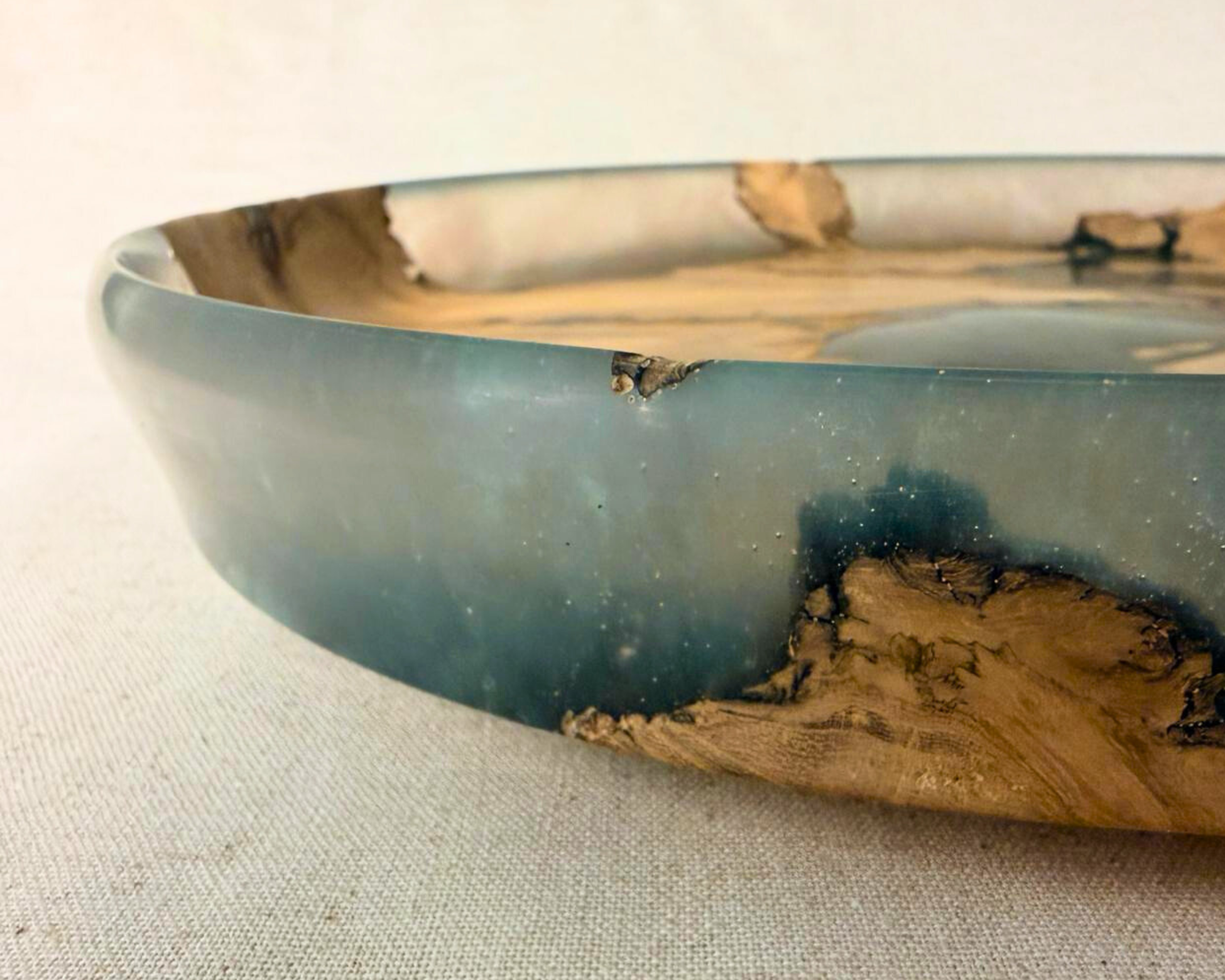 Side edge detail of tree root epoxy platter showing smoky blue resin and embedded wood at the perimeter.