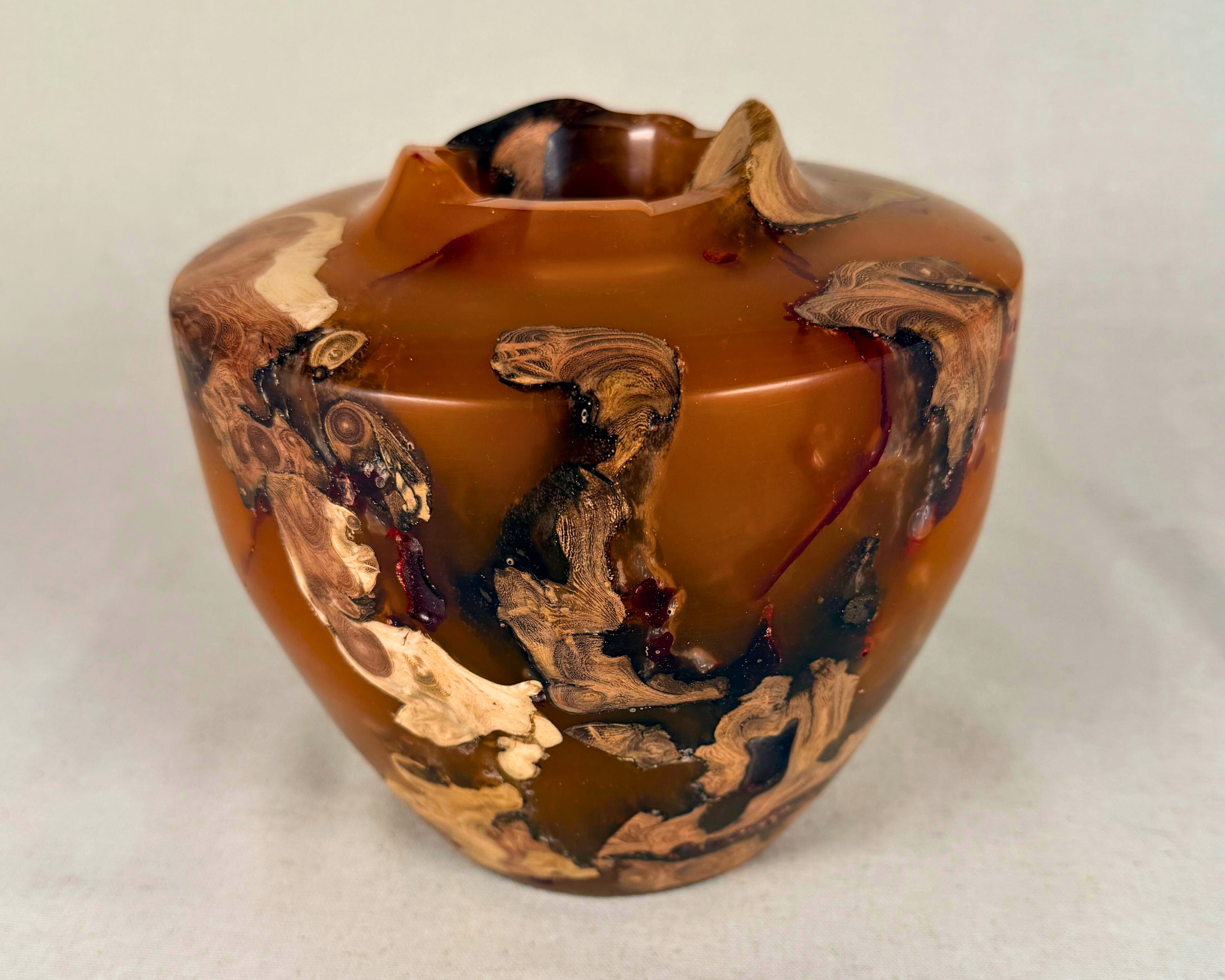 Angled view of a driftwood and amber epoxy vessel with natural inclusions, soft translucency, and a carved opening, styled as collectible wood and resin art.
