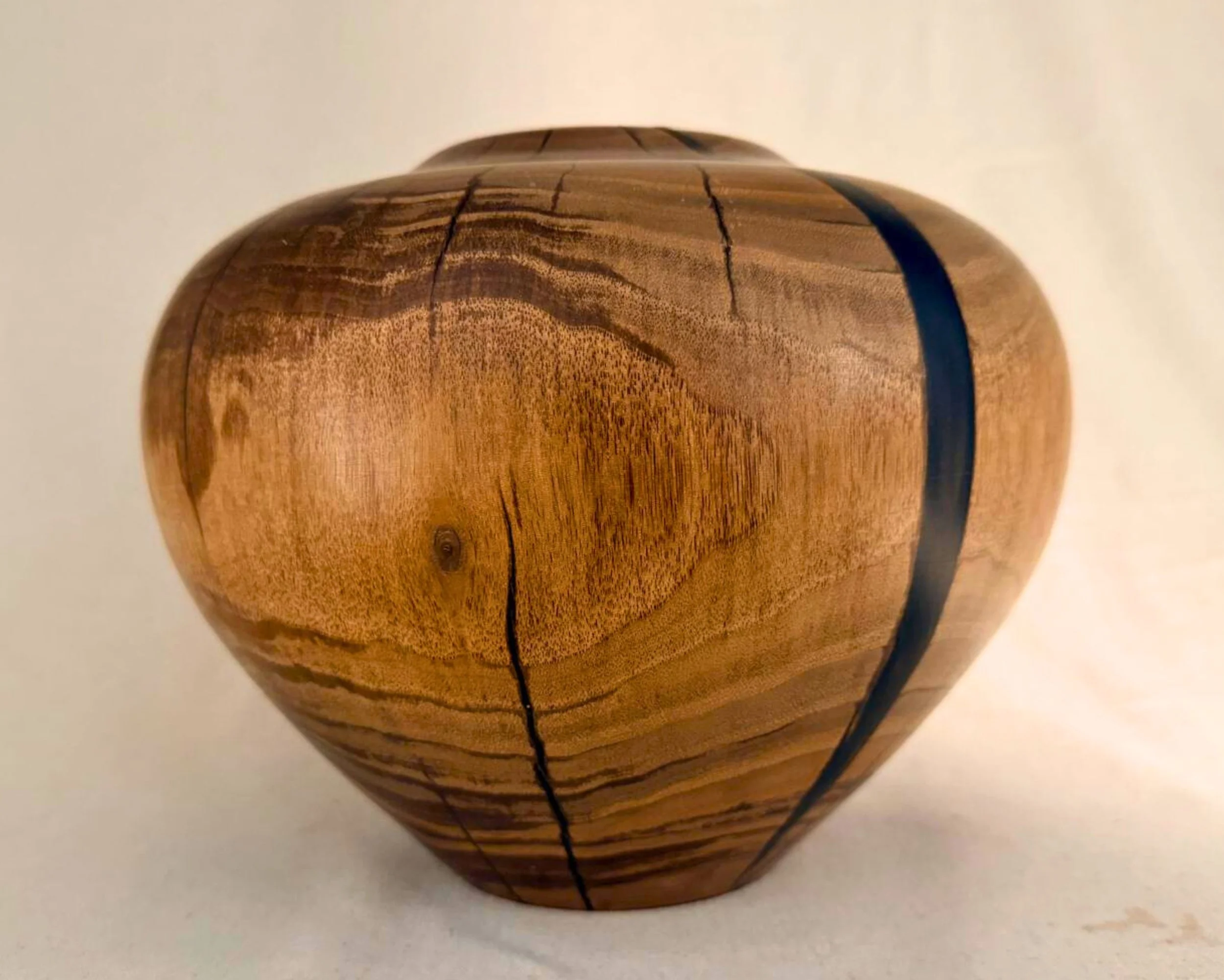Side profile of walnut vessel with dark epoxy vein and visible growth-ring movement wrapping the form.