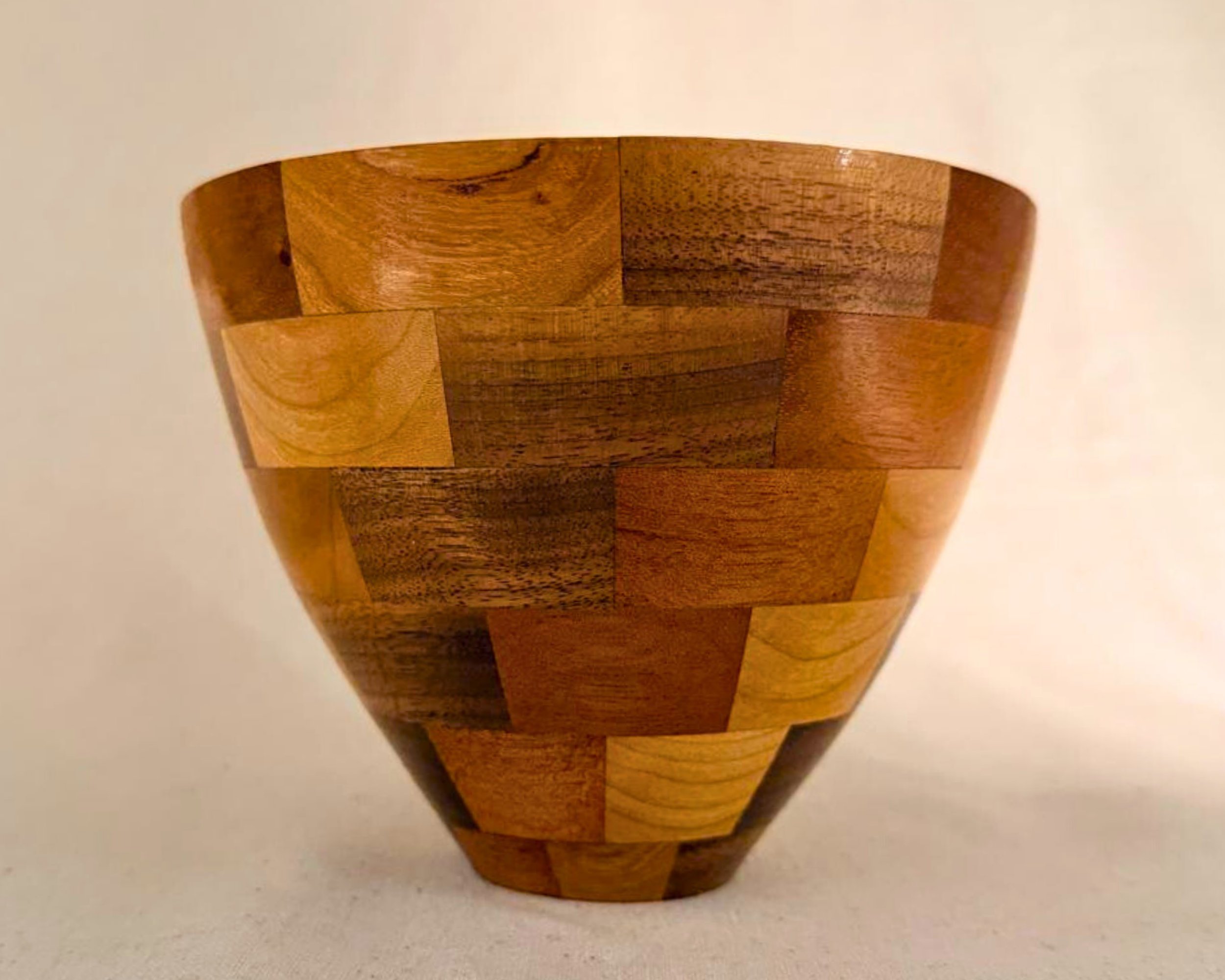 Segmented wood vessel in walnut, padauk, and maple showing warm contrast blocks, angled view.