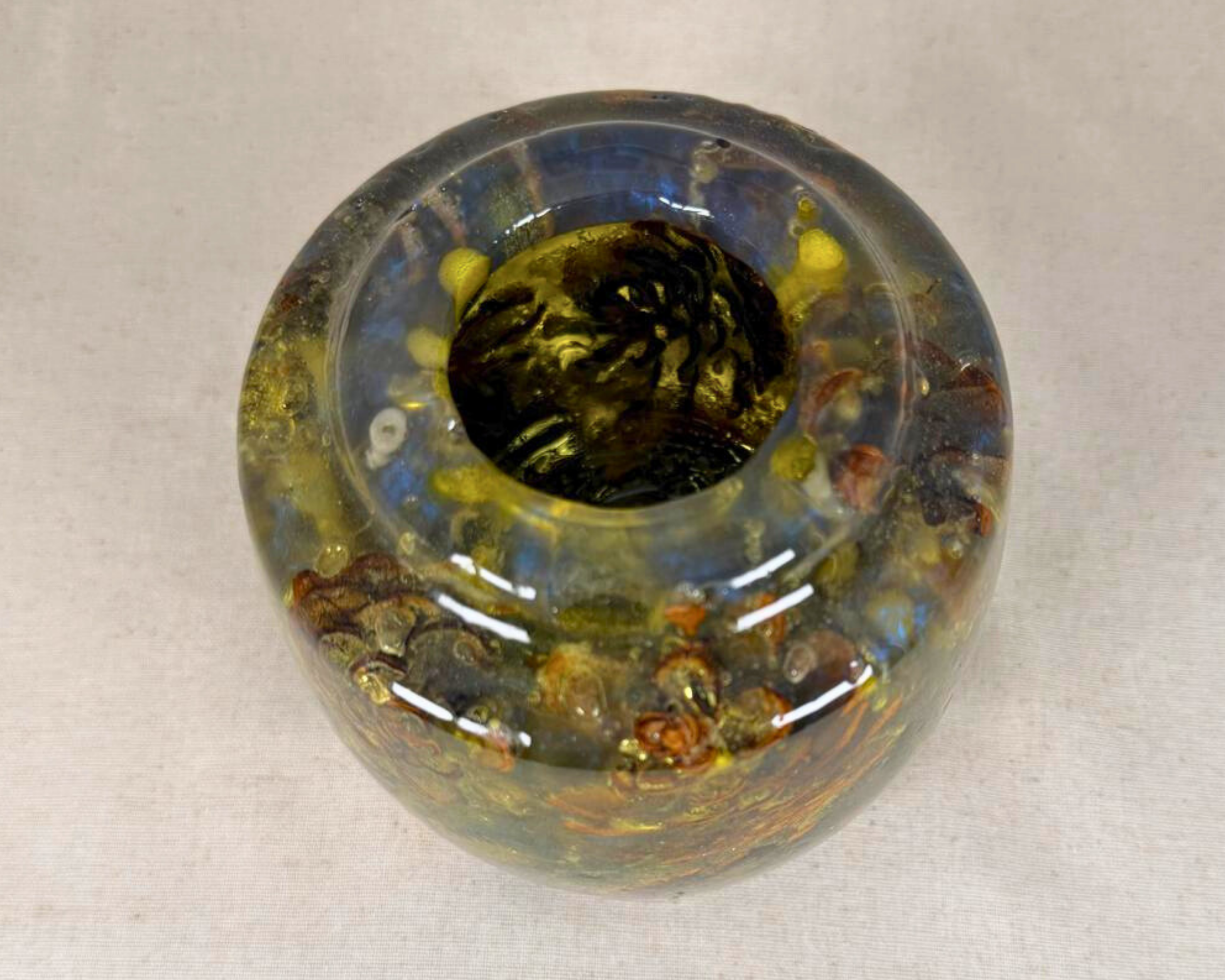 Overhead view of the vessel with a rounded rim, dark interior opening, and multicolored epoxy in smoky blue, olive, and amber tones.