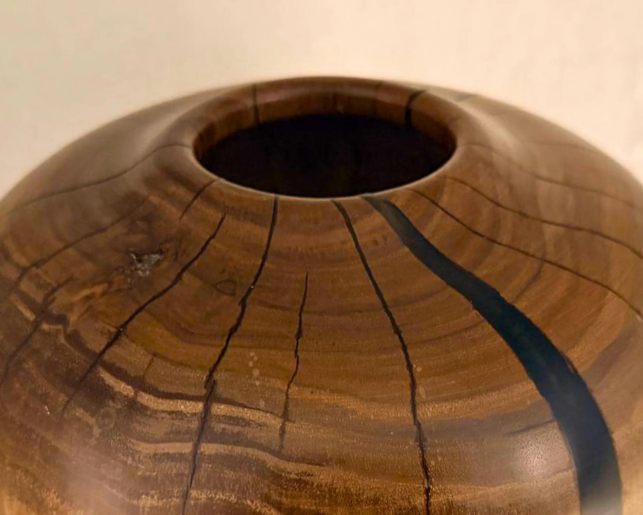 Close-up angled view of walnut vessel rim and shoulder showing dark epoxy vein and fine checking lines.